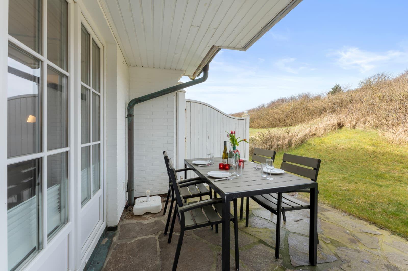Terrasse mit Tisch und Stühlen, Blick auf Gras und Hügel.