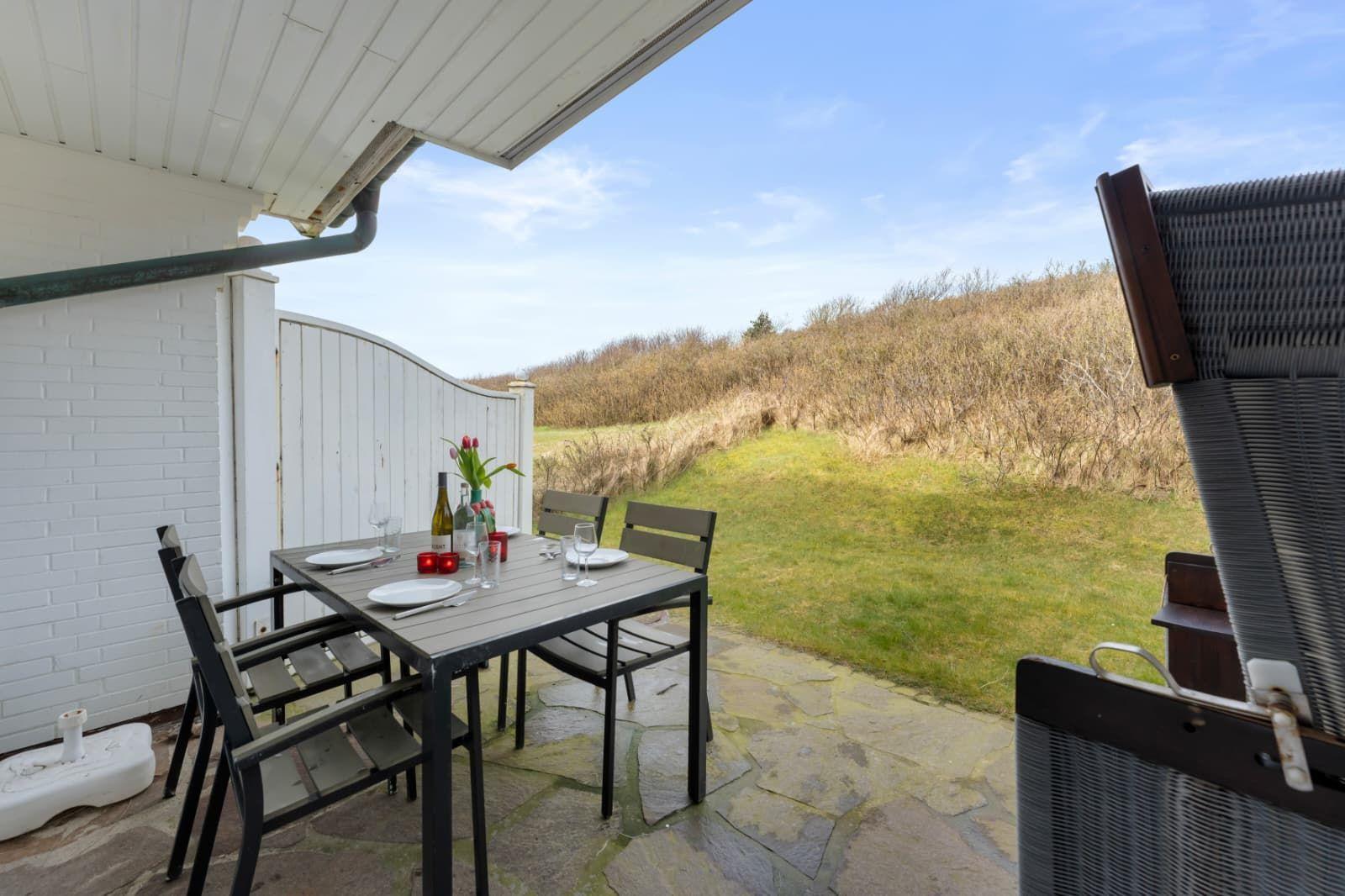 Terrasse mit Tisch und Stühlen, Blick auf grünen Hang.