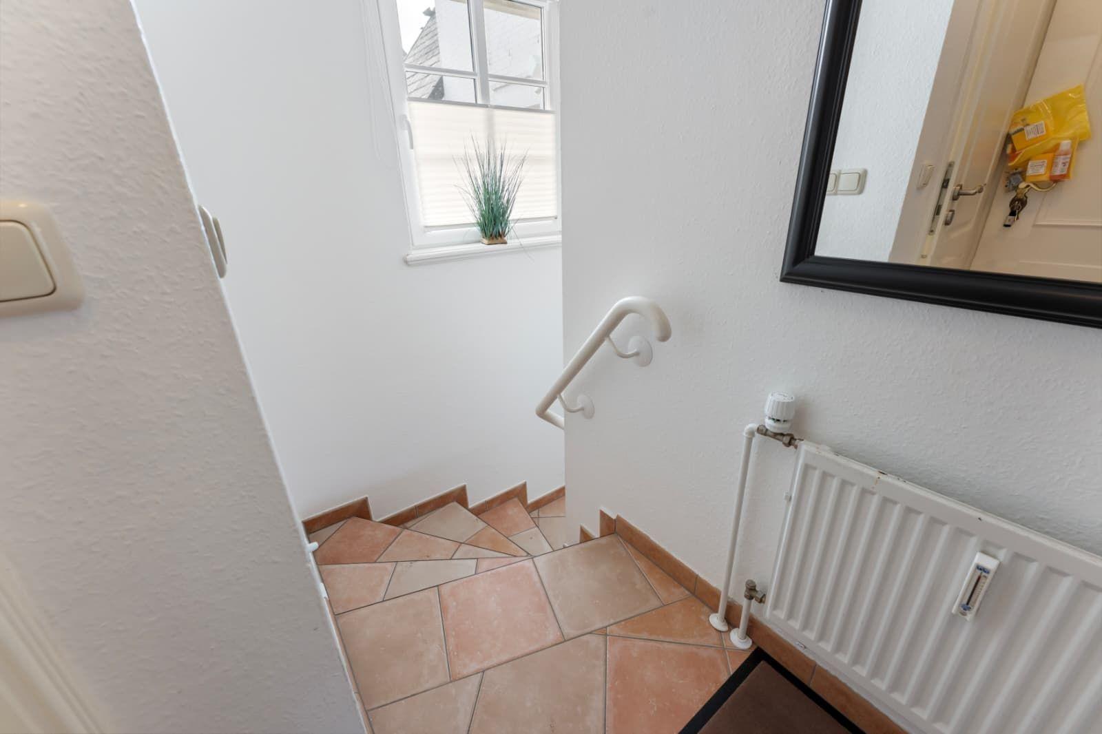 Treppe mit Handlauf, Fenster mit Pflanze und Spiegel an der Wand.