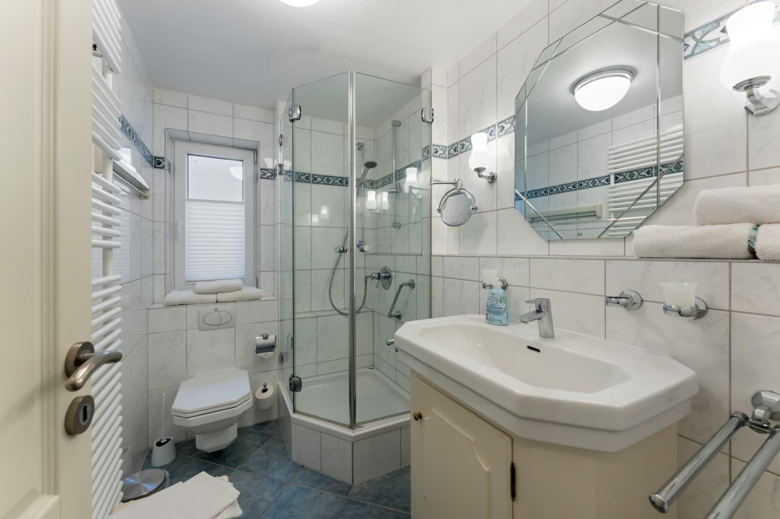 Badezimmer mit Dusche, Waschbecken und Toilette. Fliesen und Spiegel sichtbar.