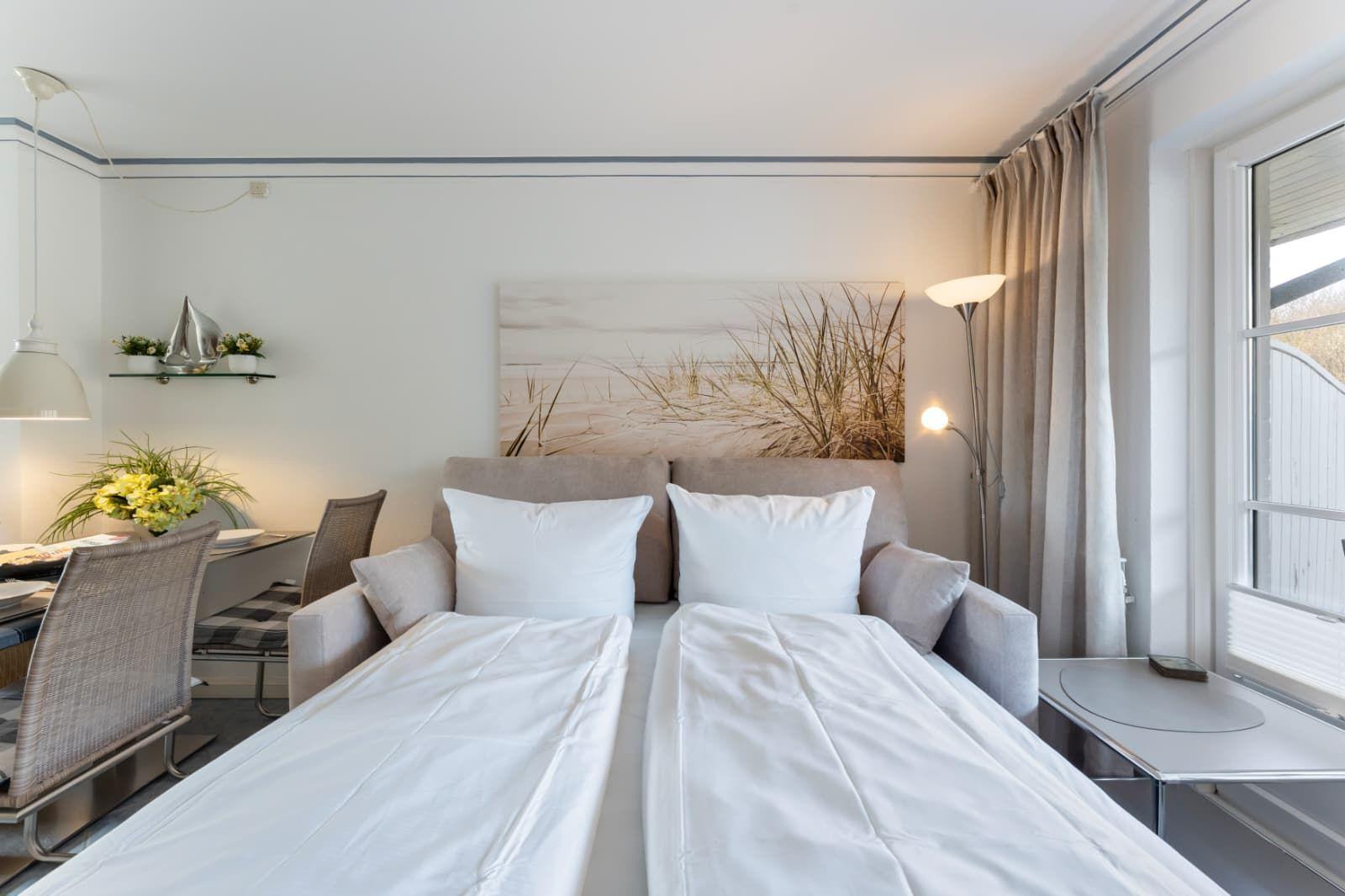 Zimmer mit Doppelbett, Wandbild, Tisch und Stühle. Fenster mit Vorhängen.