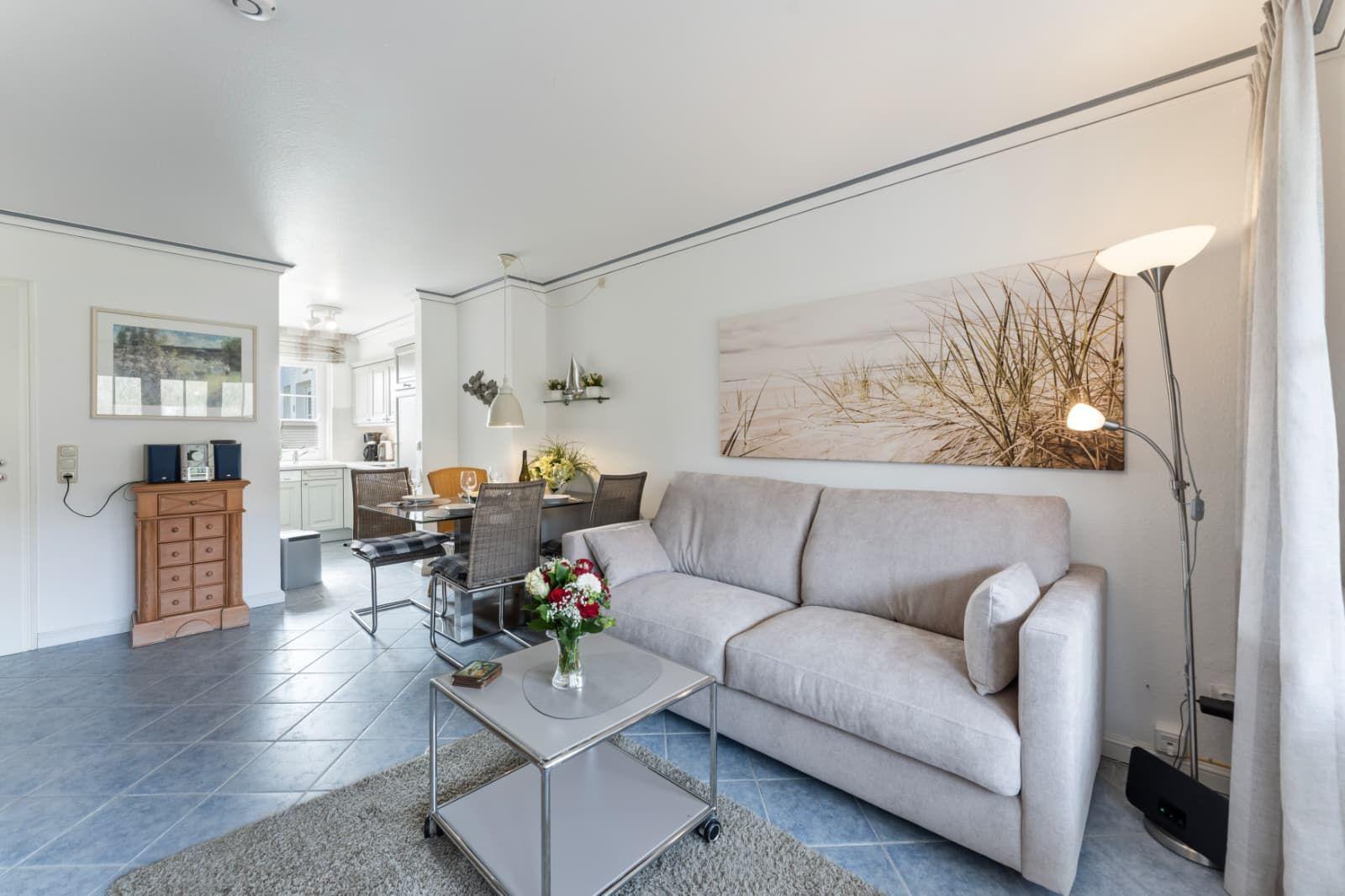 Wohnzimmer mit Sofa, Couchtisch und Wandbild. Im Hintergrund ist Essbereich und Küche.