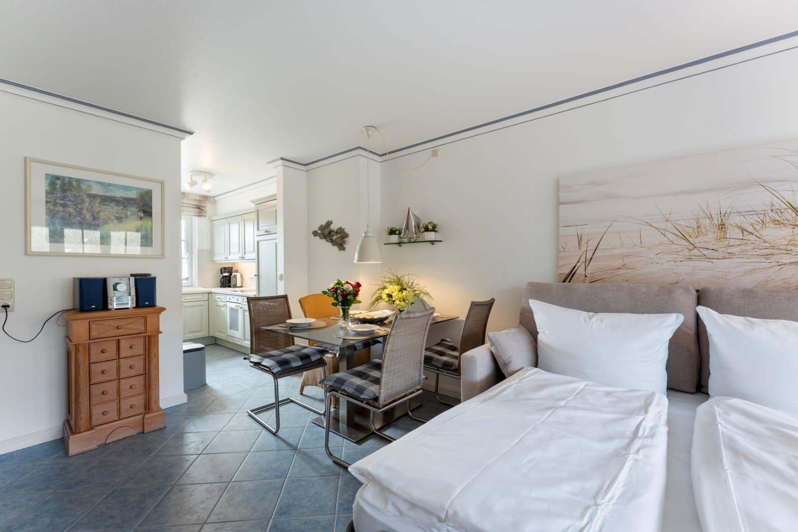 Schlafzimmer mit Bett, Essbereich und Küchenbereich. Wandbild und Holzschrank sind sichtbar.