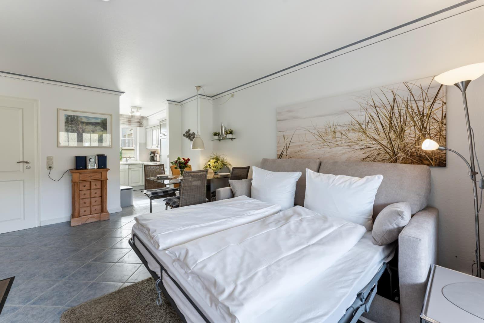 Schlafzimmer mit Bett, Wandbild und Sitzgelegenheit im Hintergrund.