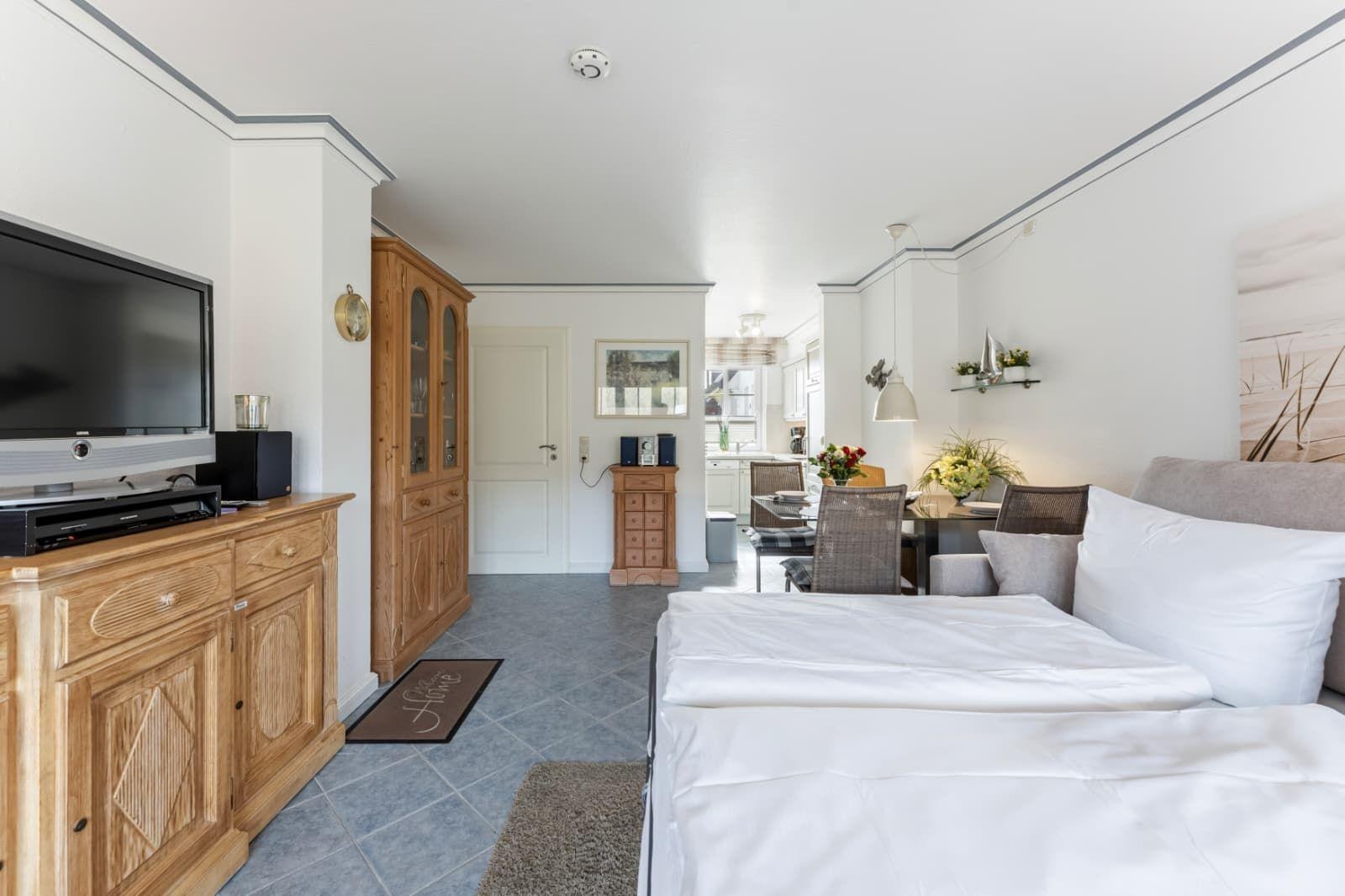 Schlafzimmer mit Bett, TV und Küchenbereich im Hintergrund.