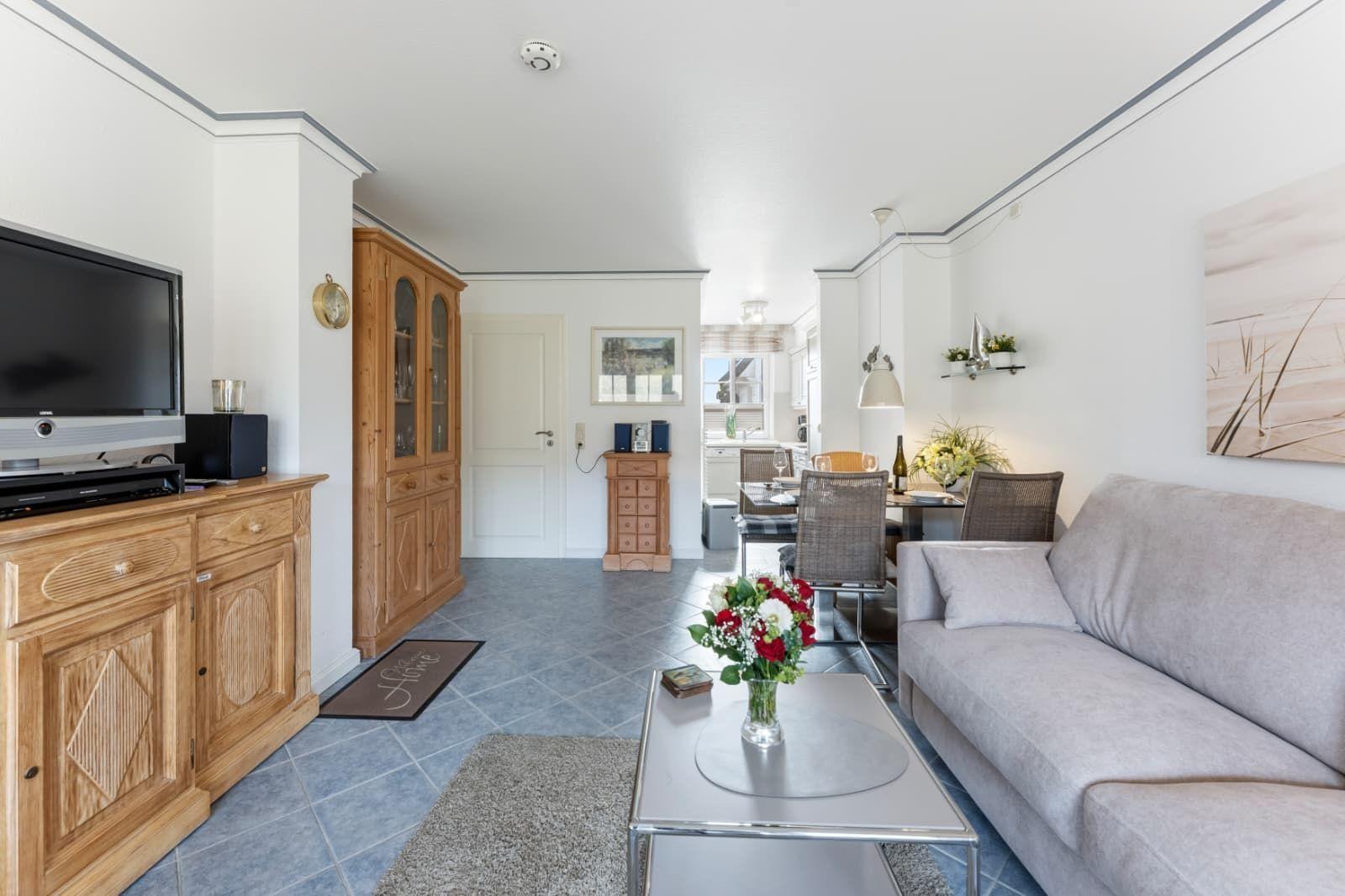 Wohn- und Essbereich mit Sofa, Couchtisch und TV. Holzmöbel und Blumen dekorieren den Raum.