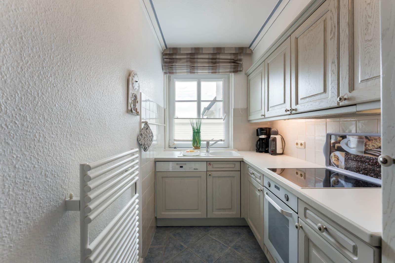 Küche mit weißen Schränken, Spüle, Fenster und Küchengeräten.