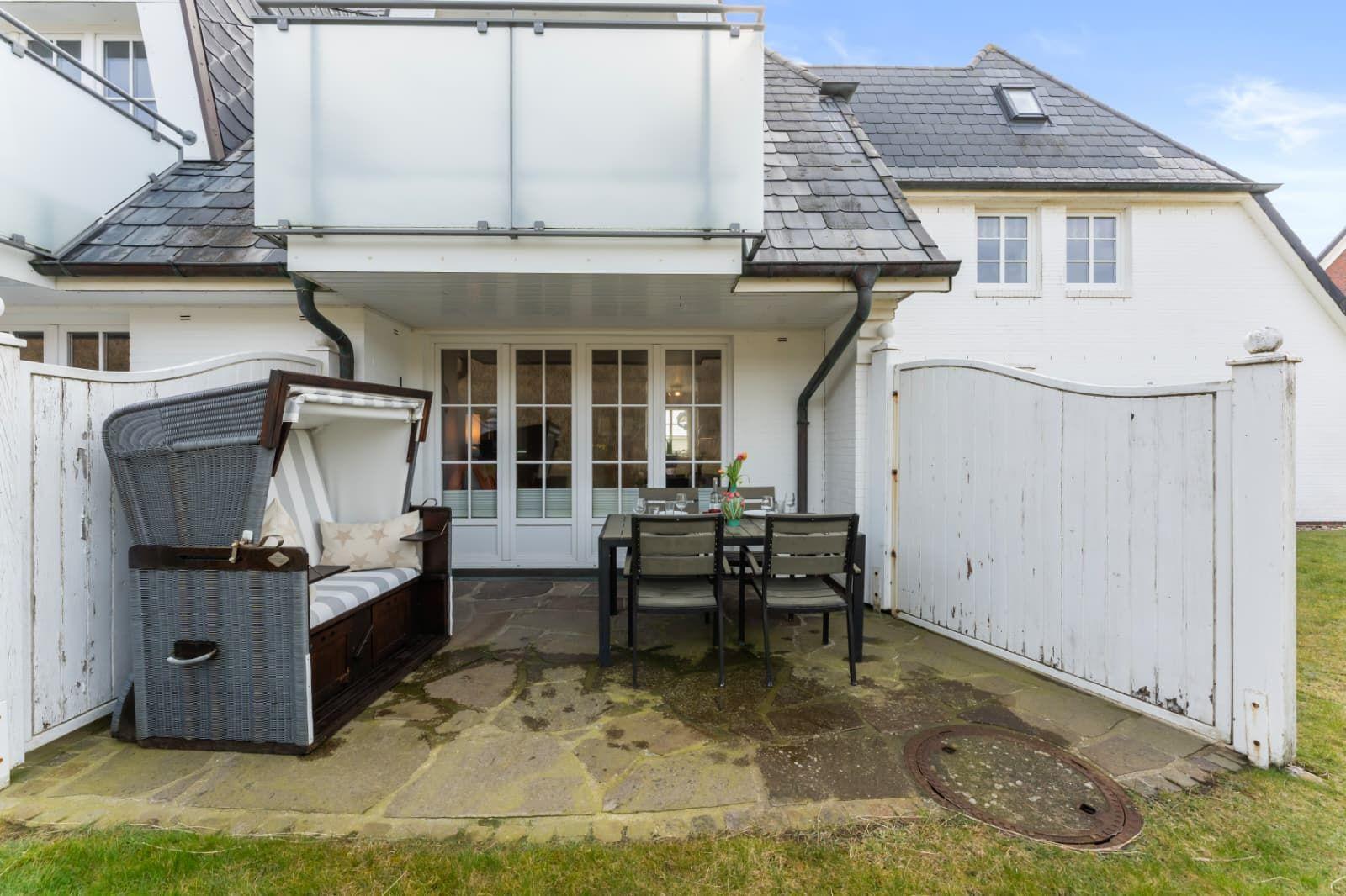Terrasse mit Sitzgruppe, Gartentisch und weißer Hauswand.