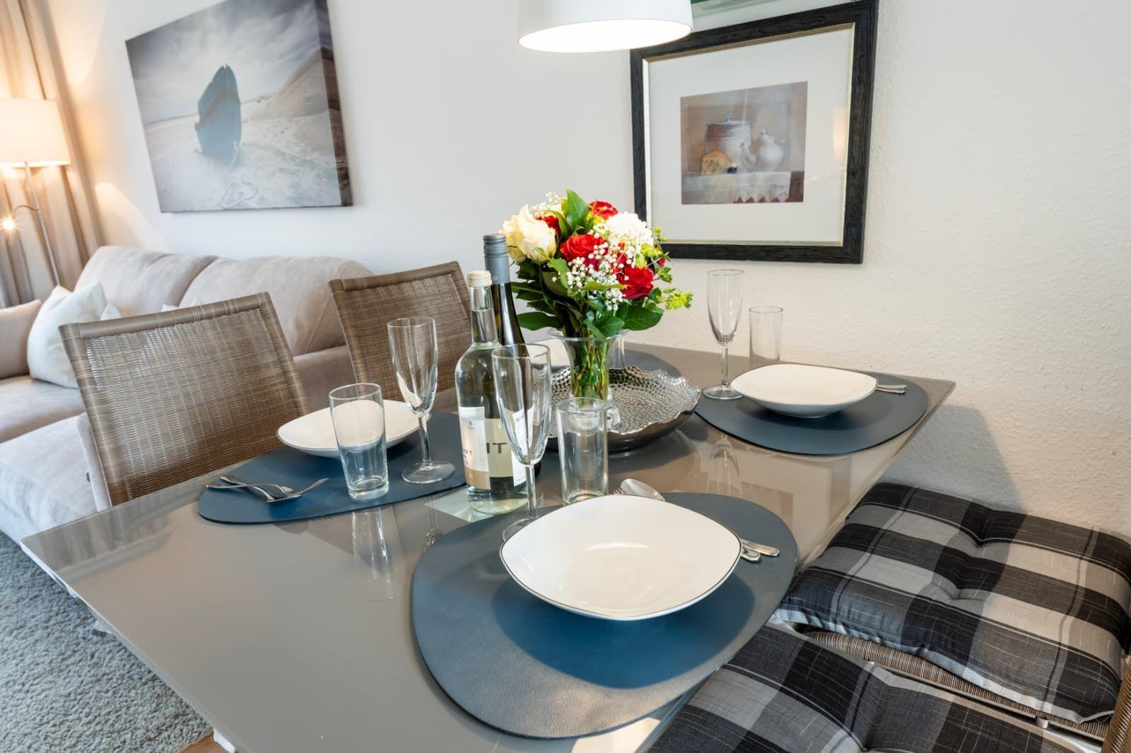 Dining table set for four with vase and bottle on the tabletop.