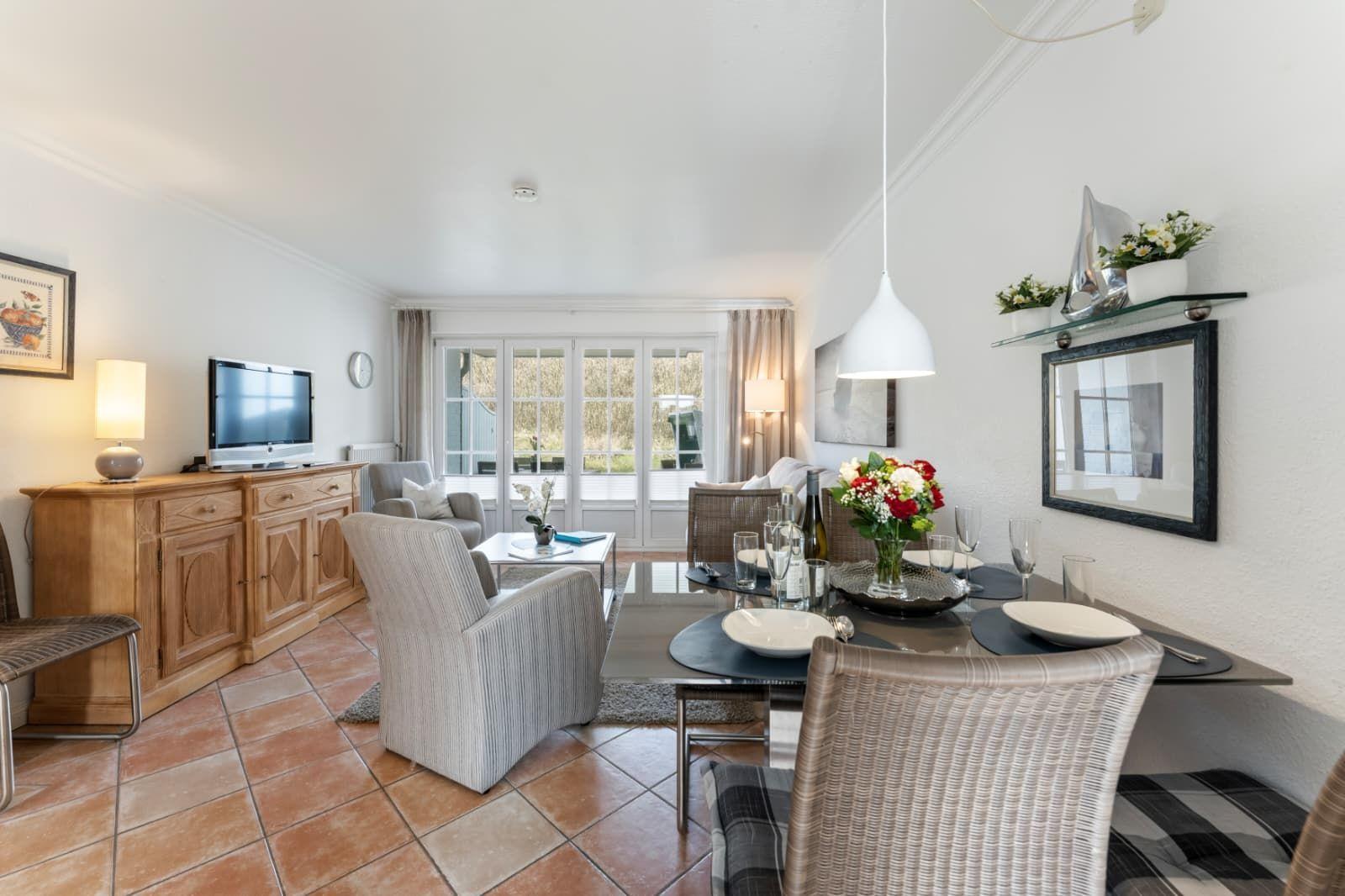 Living and dining area with TV, dining table, and windows to the outdoor terrace.