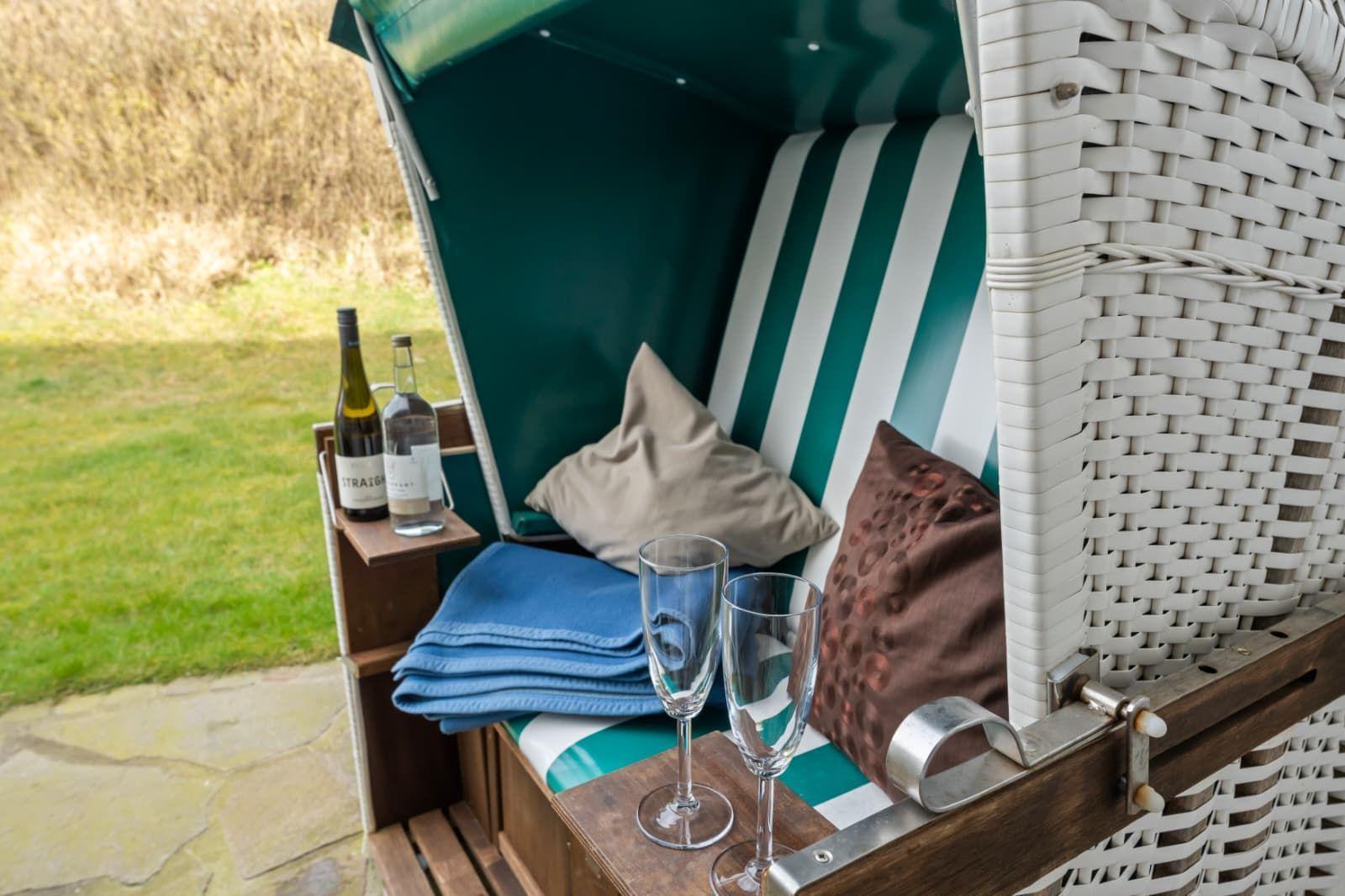 Green beach chair with cushions, blanket, and glasses. Background: grass and stone path.