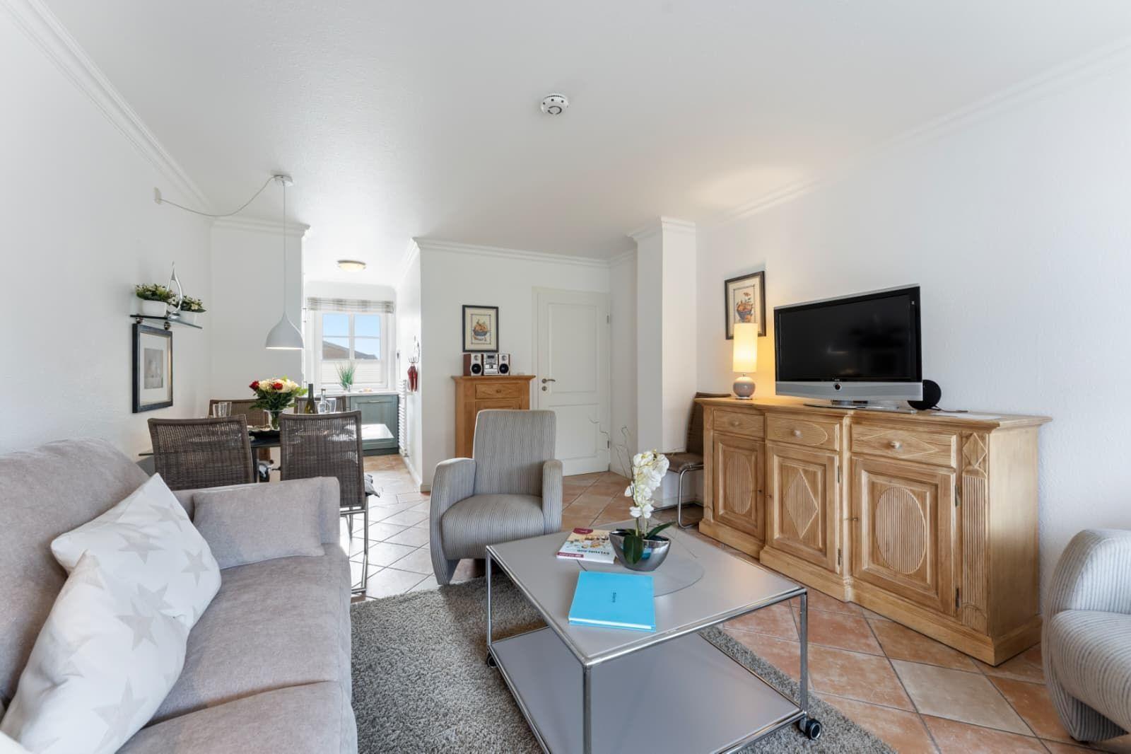 Living room with sofa, TV, and dining area. Wooden furniture and terracotta floor.