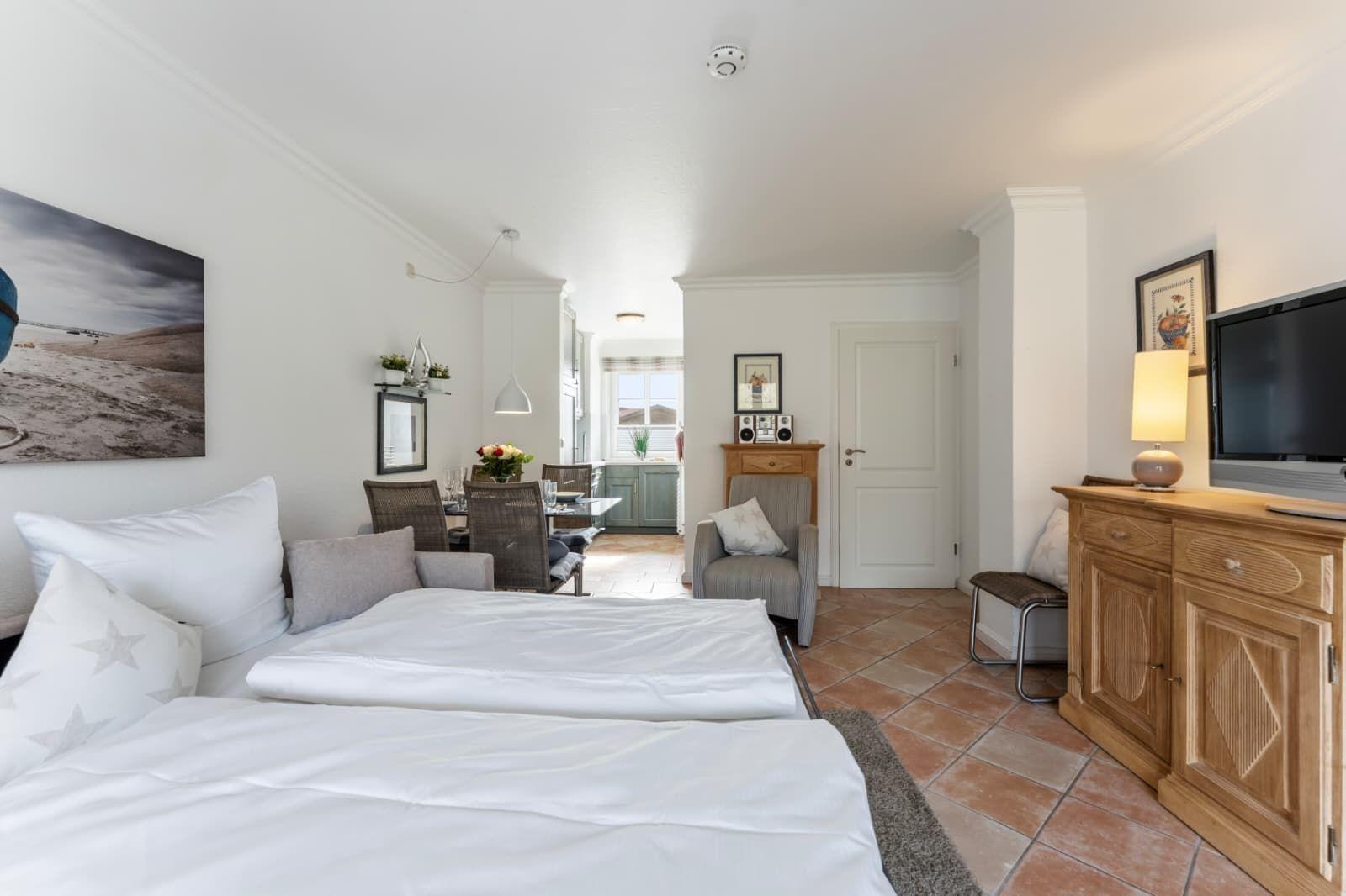 Bedroom with double bed, living area, and kitchen in the background.