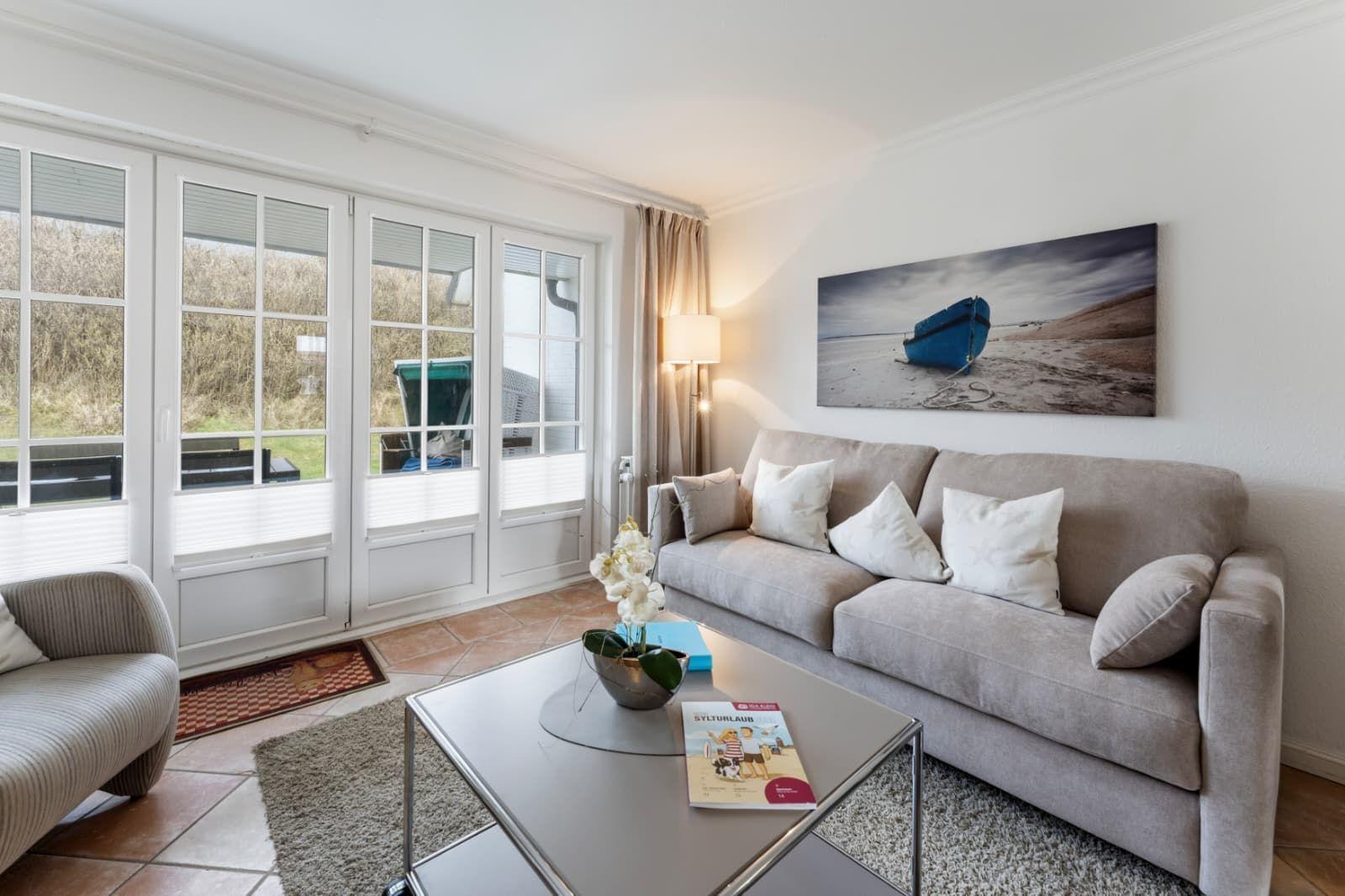 Living room with sofa, coffee table, and large windows. Wall art shows a blue boat.