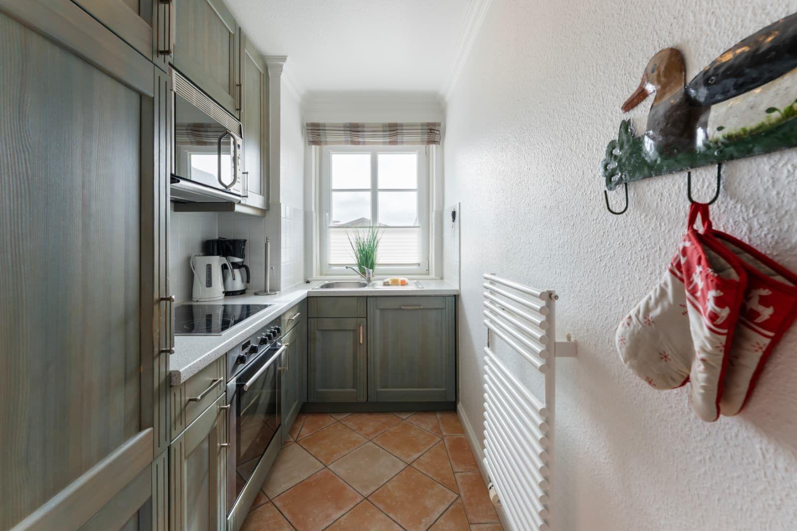 Kitchen with gray cabinets, stove, and window. Oven mitts and a duck hang on the wall.
