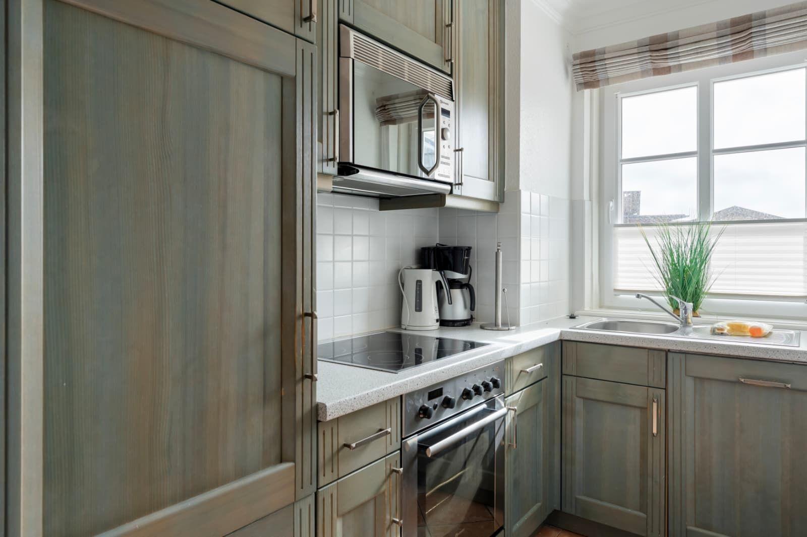 Kitchen with gray cabinets, stove, microwave, and window with plant.