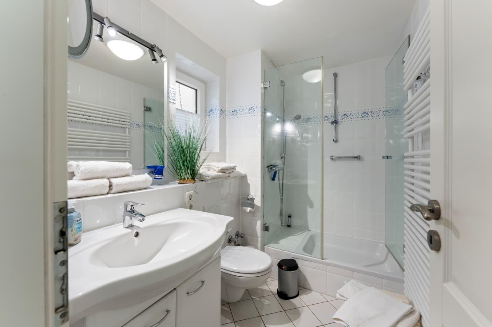 Bathroom with shower, sink, and toilet. White tiles and towels.