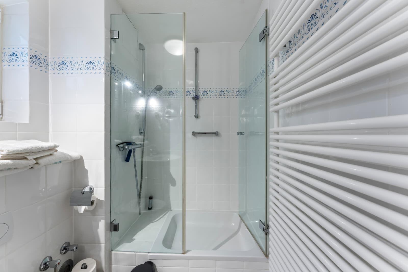 Shower with glass enclosure, white tiles, and heater.