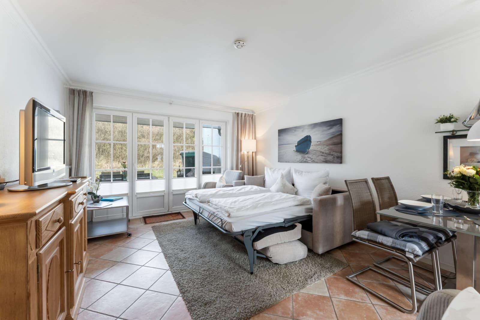 Living room with sofa bed, dining table and TV. Large window front with view outside.