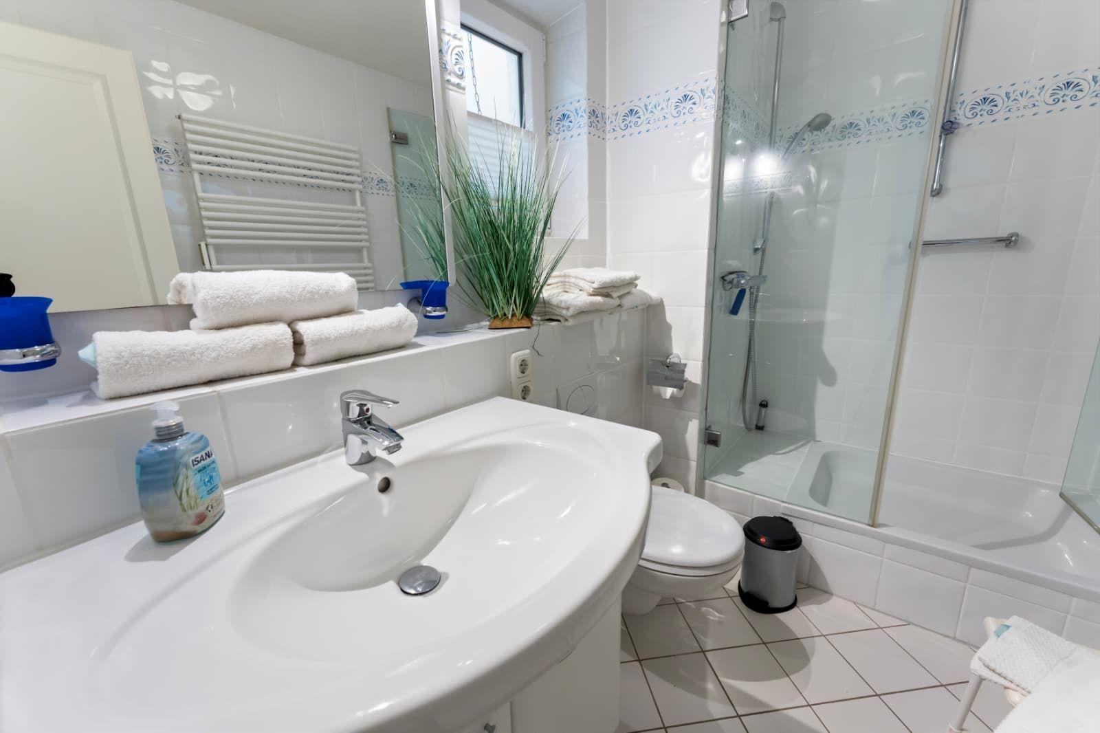 Bathroom with shower, sink, and toilet. White tiles and towels.
