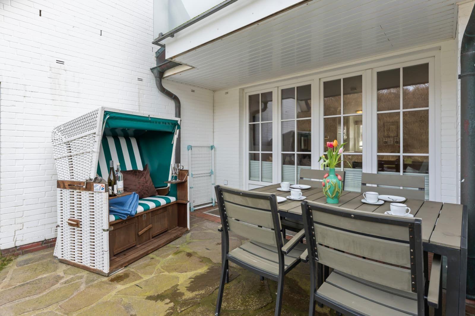 Terrace with beach chair, table and chairs. White wall and windows in the background.