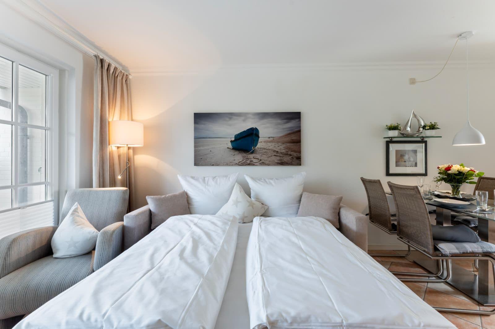 Bedroom with bed, armchair, and wall art. Adjacent dining area with table and chairs.