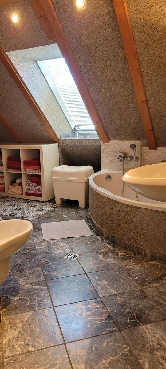 Badezimmer mit Badewanne, Waschbecken und Dusche unter Dachschrägen mit Fenster.