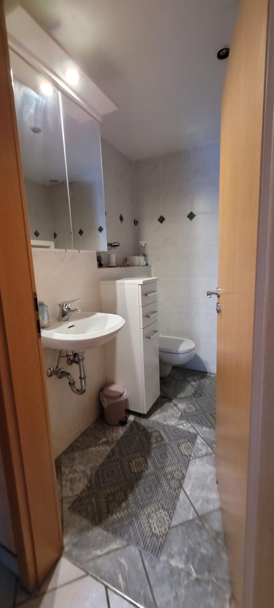 Badezimmer mit Waschbecken, Spiegelschrank, Toilette und Fliesenboden.