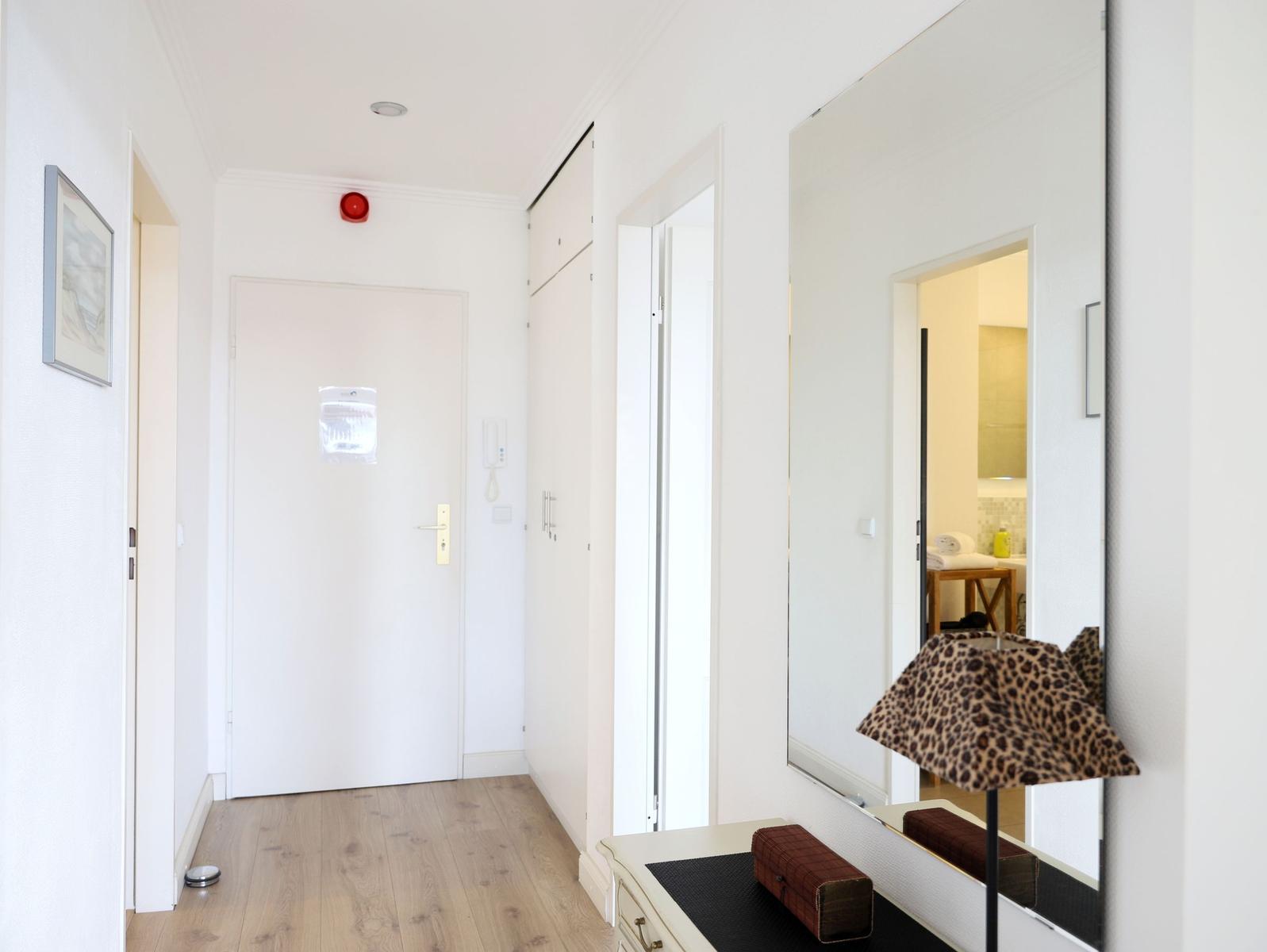 Flur mit Spiegel, Lampe und Tür. Holzfußboden und weiße Wände.