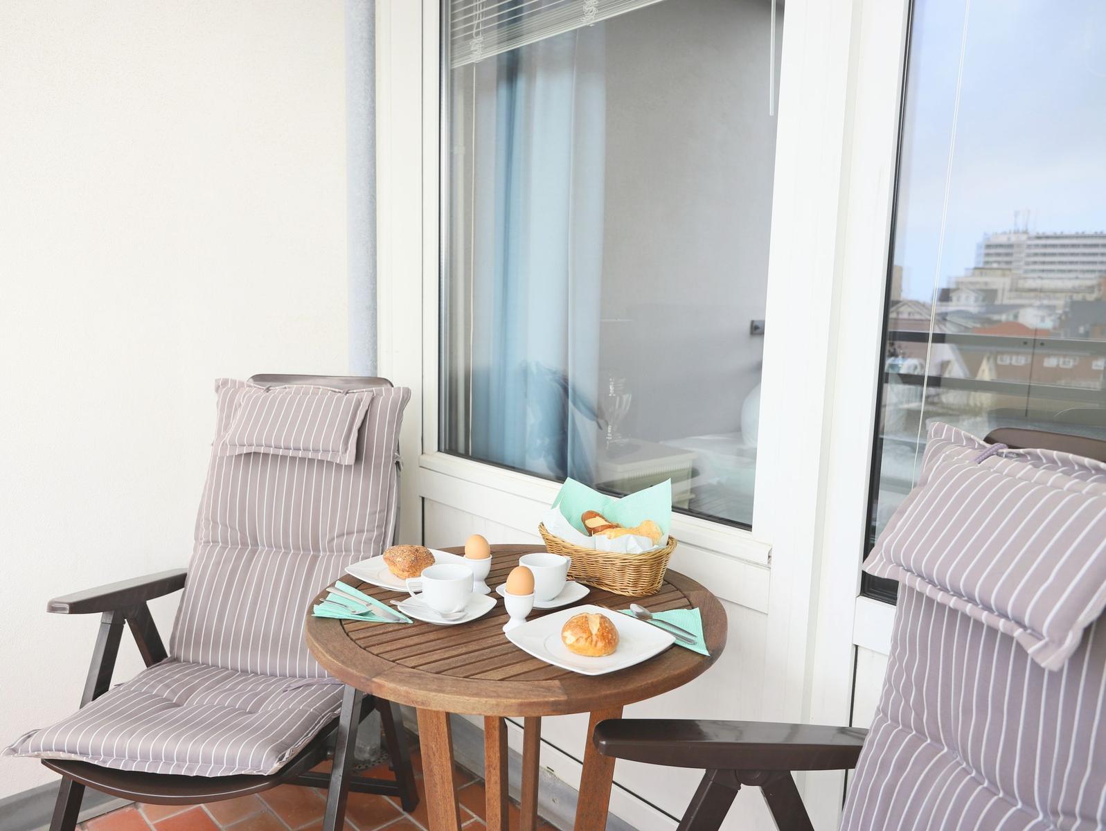Terrasse mit Tisch, zwei Stühlen und Frühstückszubehör.