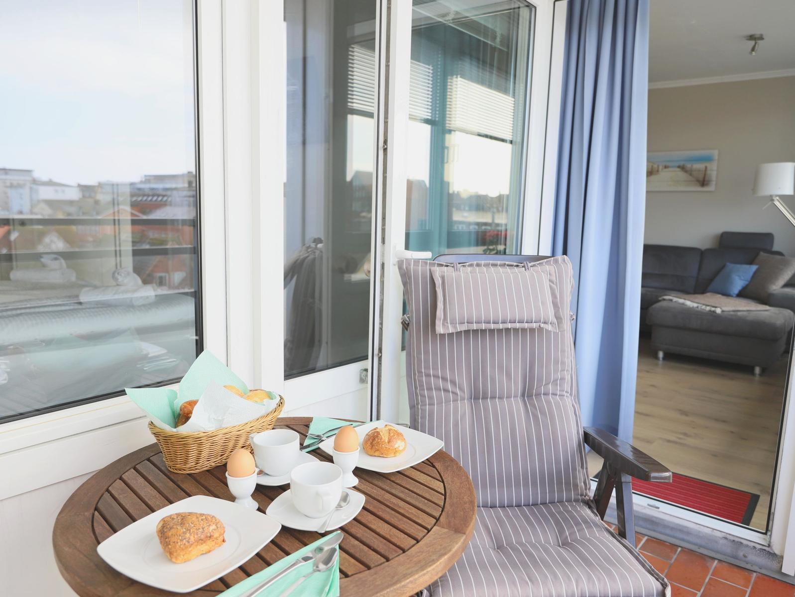 Balkon mit Tisch, Stuhl und Frühstück. Blick ins Wohnzimmer.