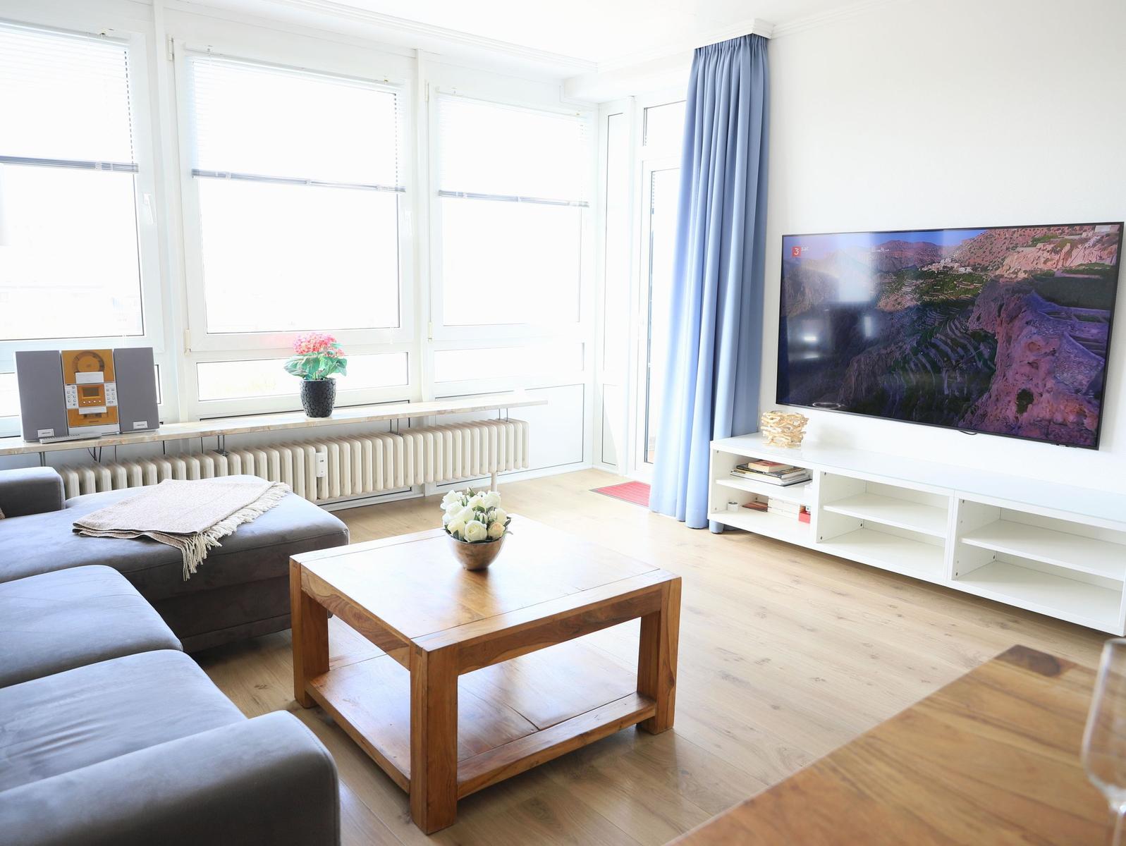 Wohnzimmer mit Sofa, Couchtisch und Fernseher an der Wand.