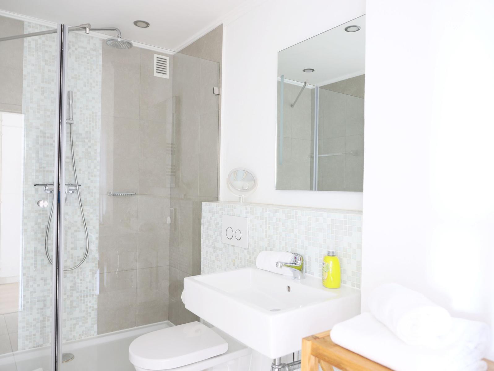 Badezimmer mit Dusche, Waschbecken und Spiegel.