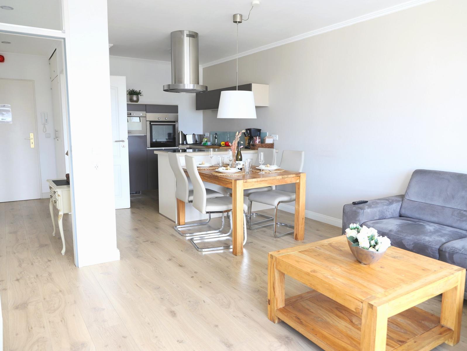 Wohn- und Essbereich mit Kücheninsel, Holztisch und grauem Sofa.