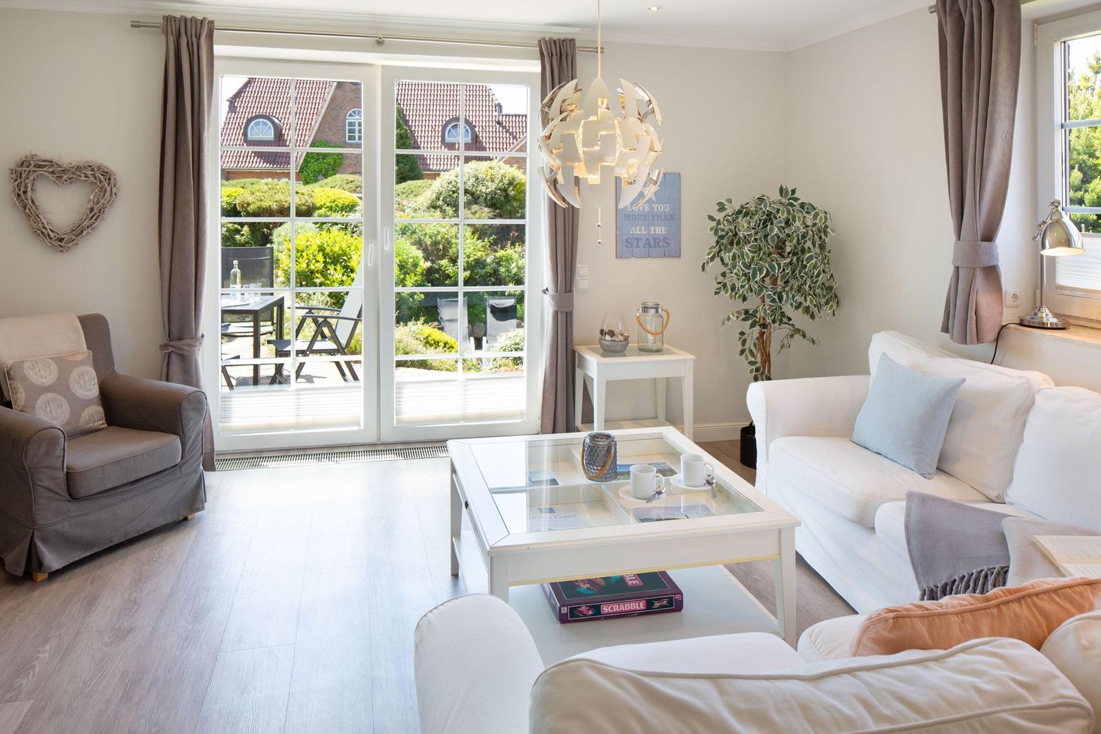 Wohnzimmer mit Sofa, Sessel und Glas-Tisch. Durchgang zur Terrasse mit Gartenansicht.