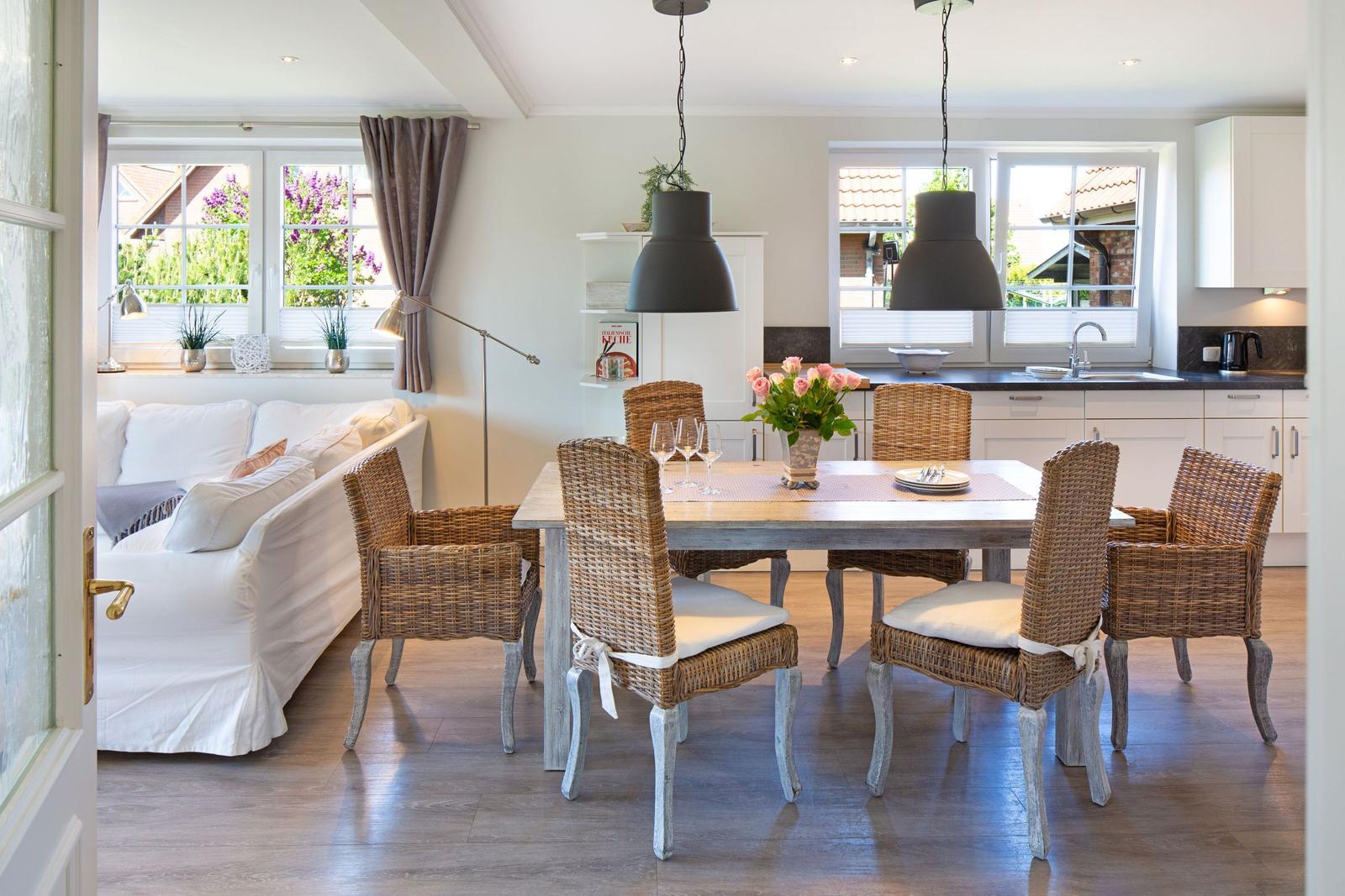Esszimmer mit Esstisch, Stühlen und Küchenbereich. Wohnbereich mit Sofa und Fenstern.