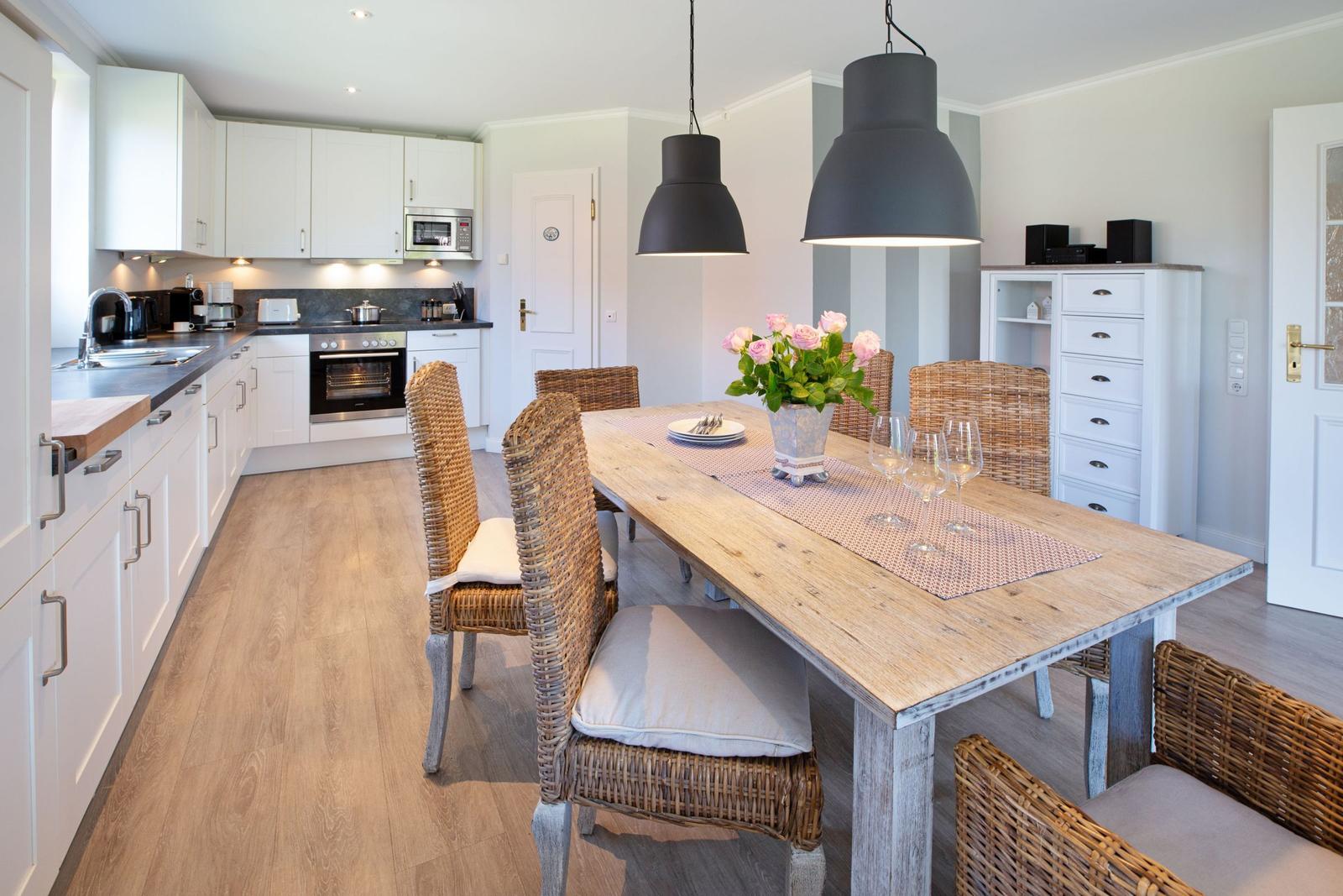 Küche und Essbereich mit Holztisch, Rattanchairs und weißen Schränken.