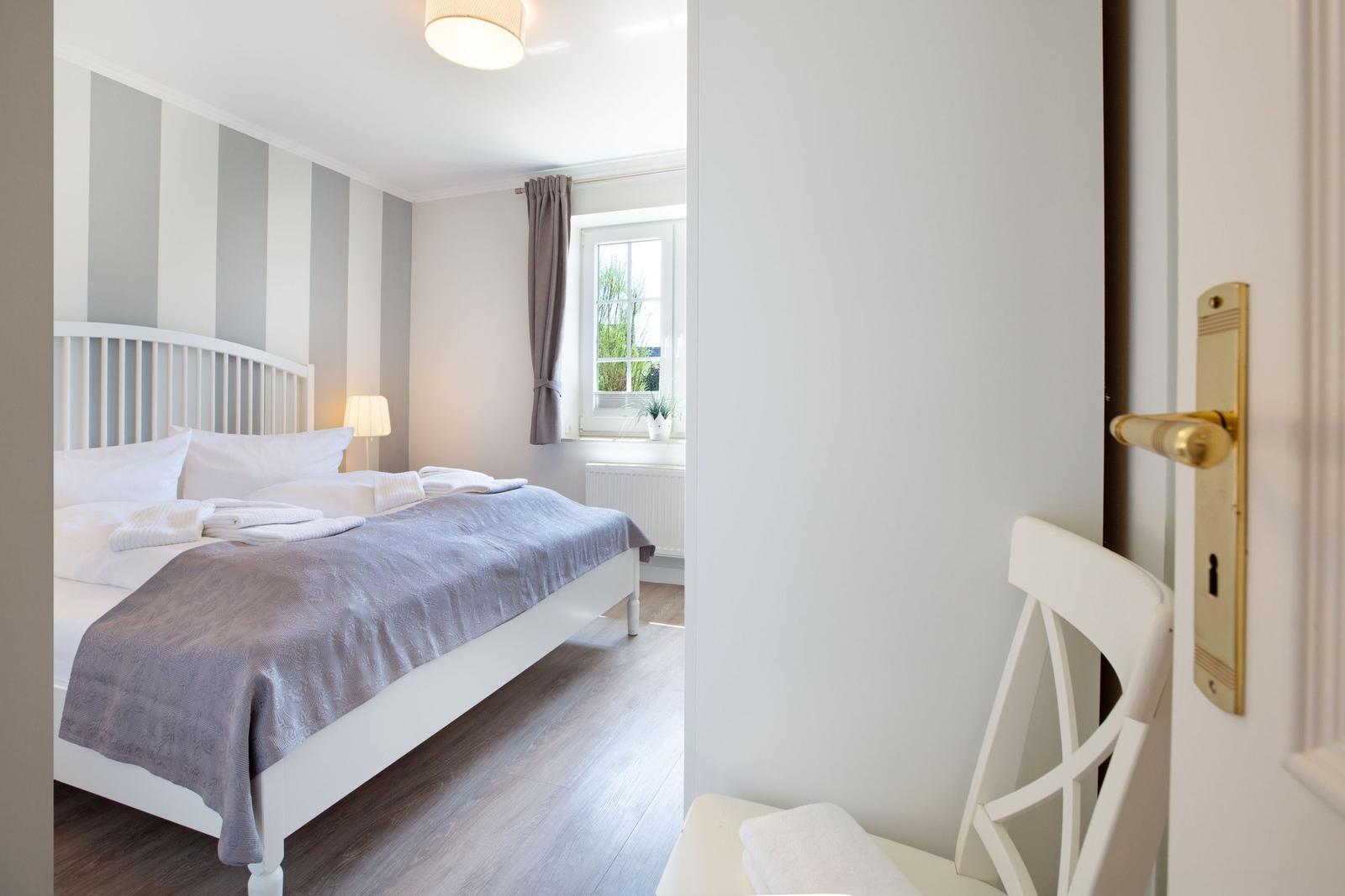 Schlafzimmer mit weißem Bett, gestreifter Wand und Fenster mit Blick nach draußen.