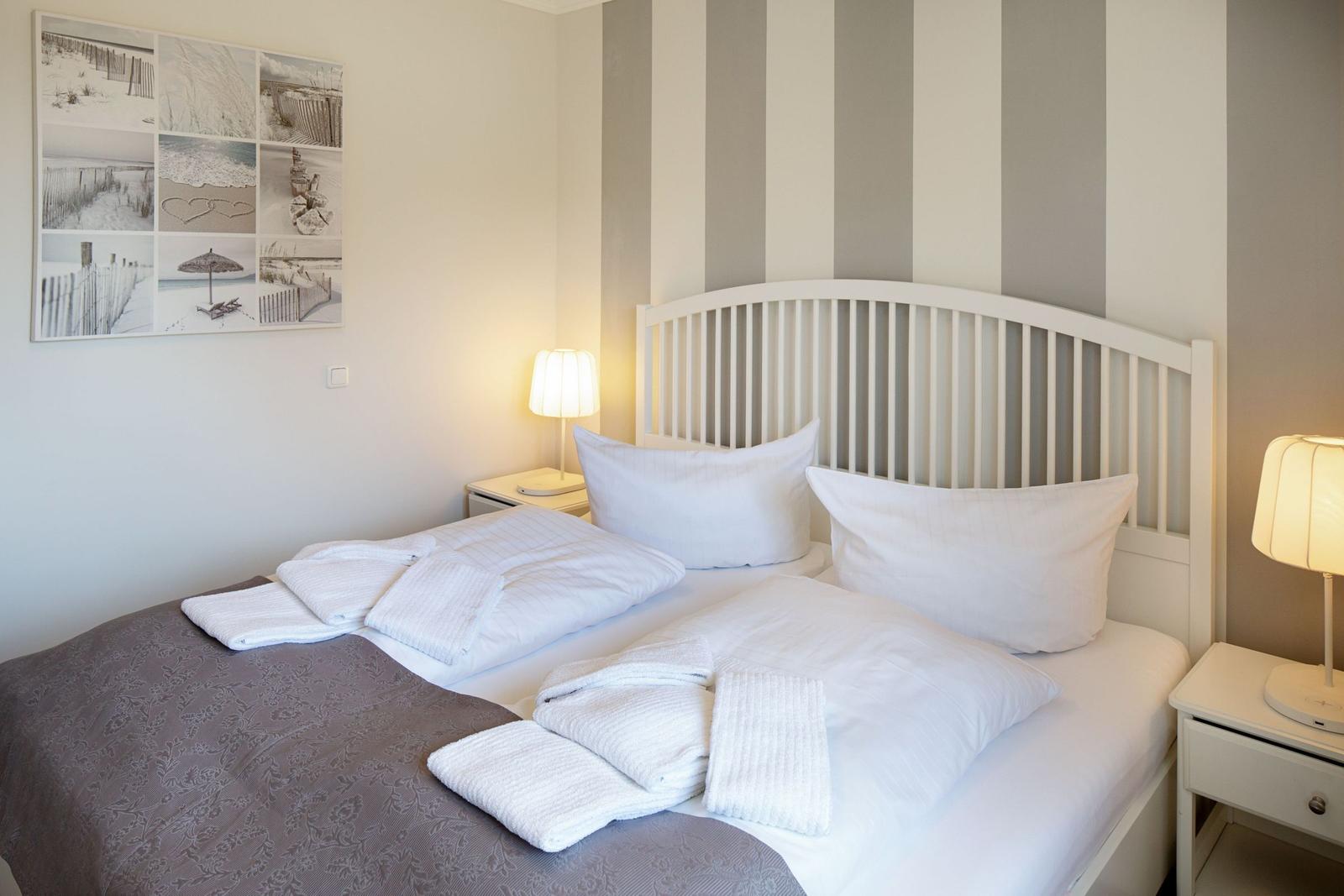 Schlafzimmer mit weißem Bett, zwei Nachttischen und Wandbildern.