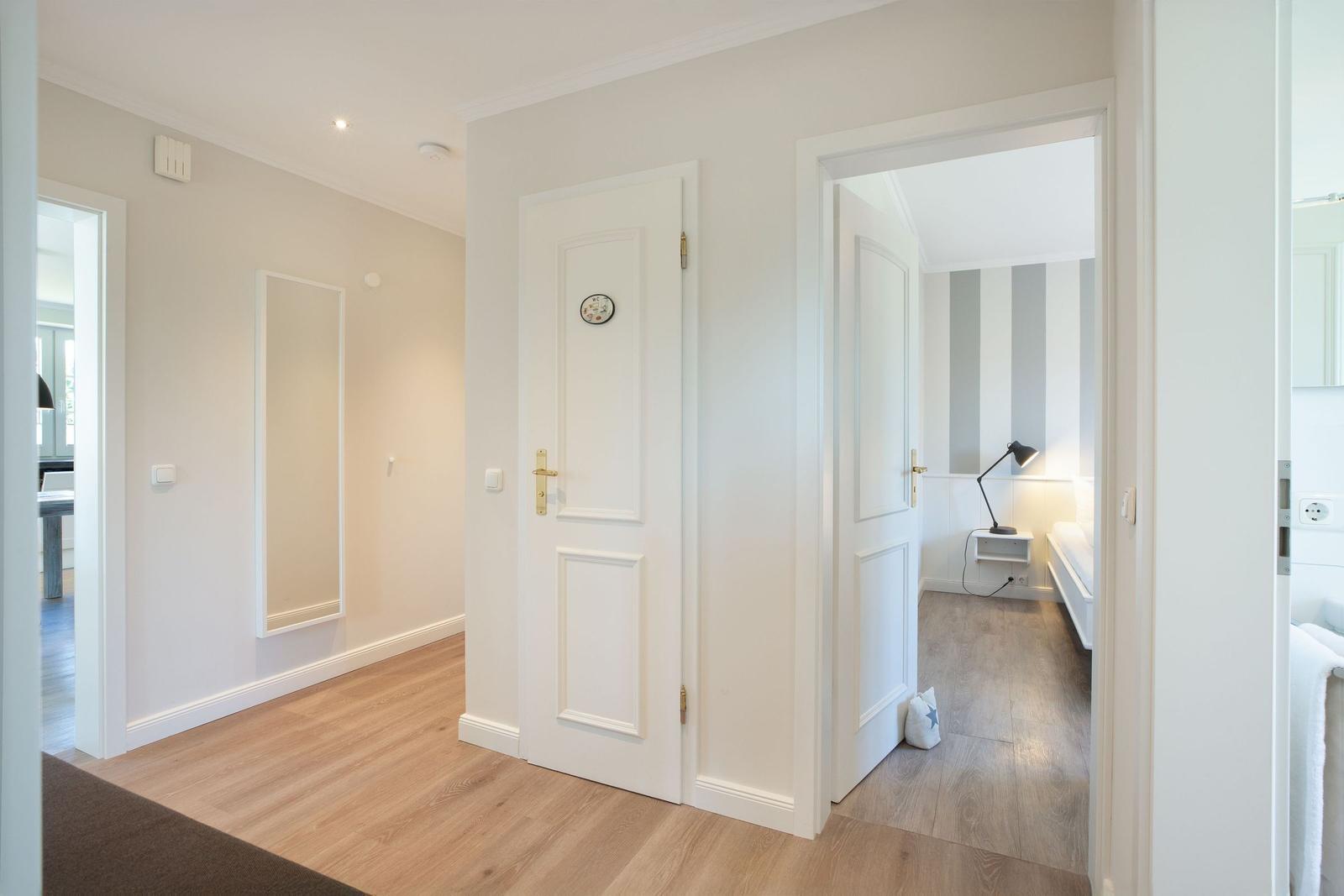 Flur mit Holzboden, weißen Türen und Blick in Schlafzimmer mit gestreifter Wand.