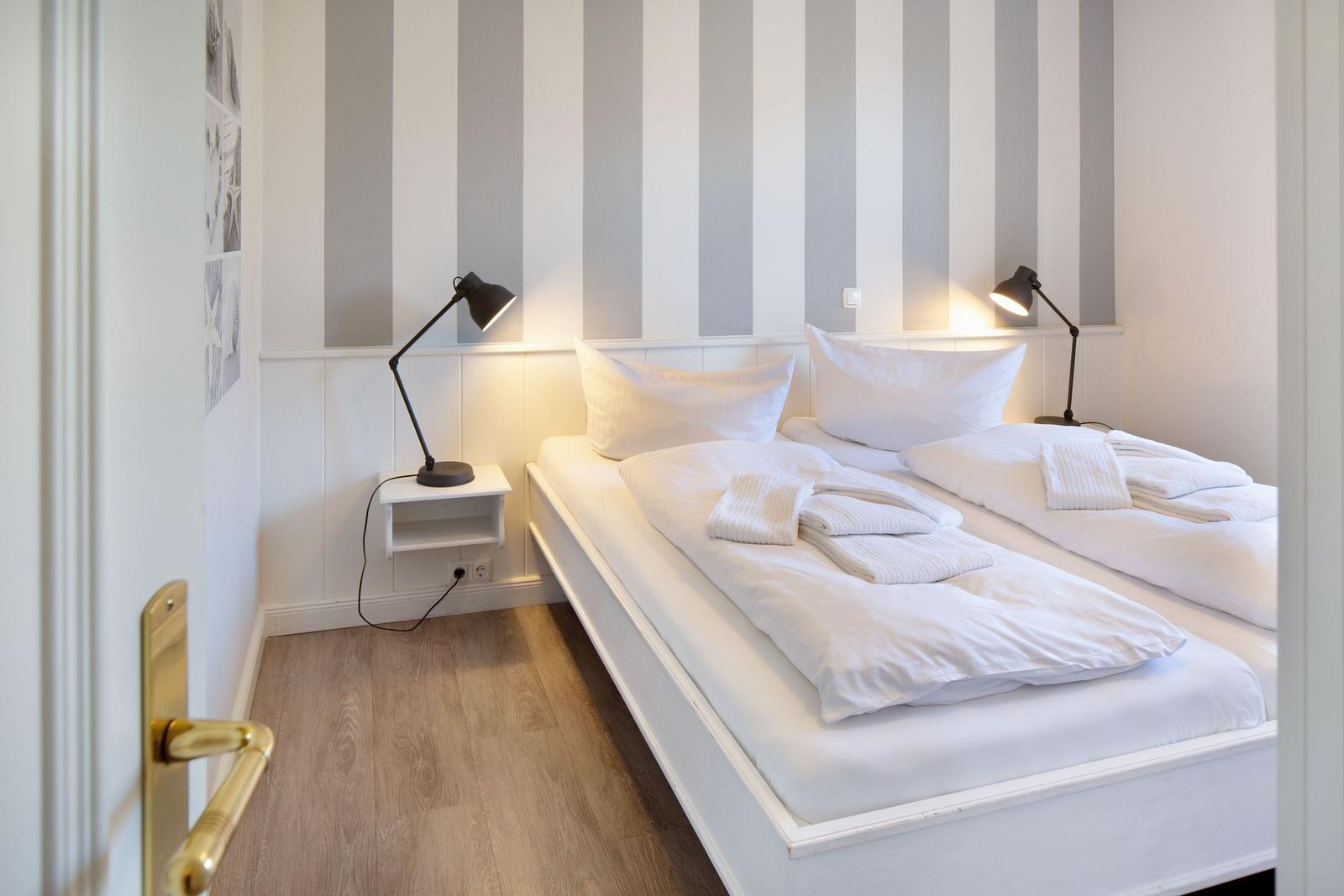 Schlafzimmer mit Doppelbett, Streifenwand und zwei Nachttischen mit Lampen.
