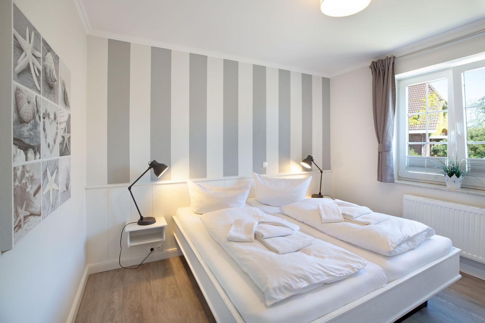 Schlafzimmer mit Doppelbett, Streifenwand und Fenster mit Blick.