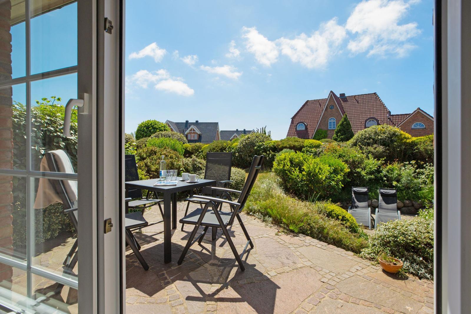 Terrasse mit Tisch und Stühlen, Blick auf begrünte Gärten und Häuser im Hintergrund.