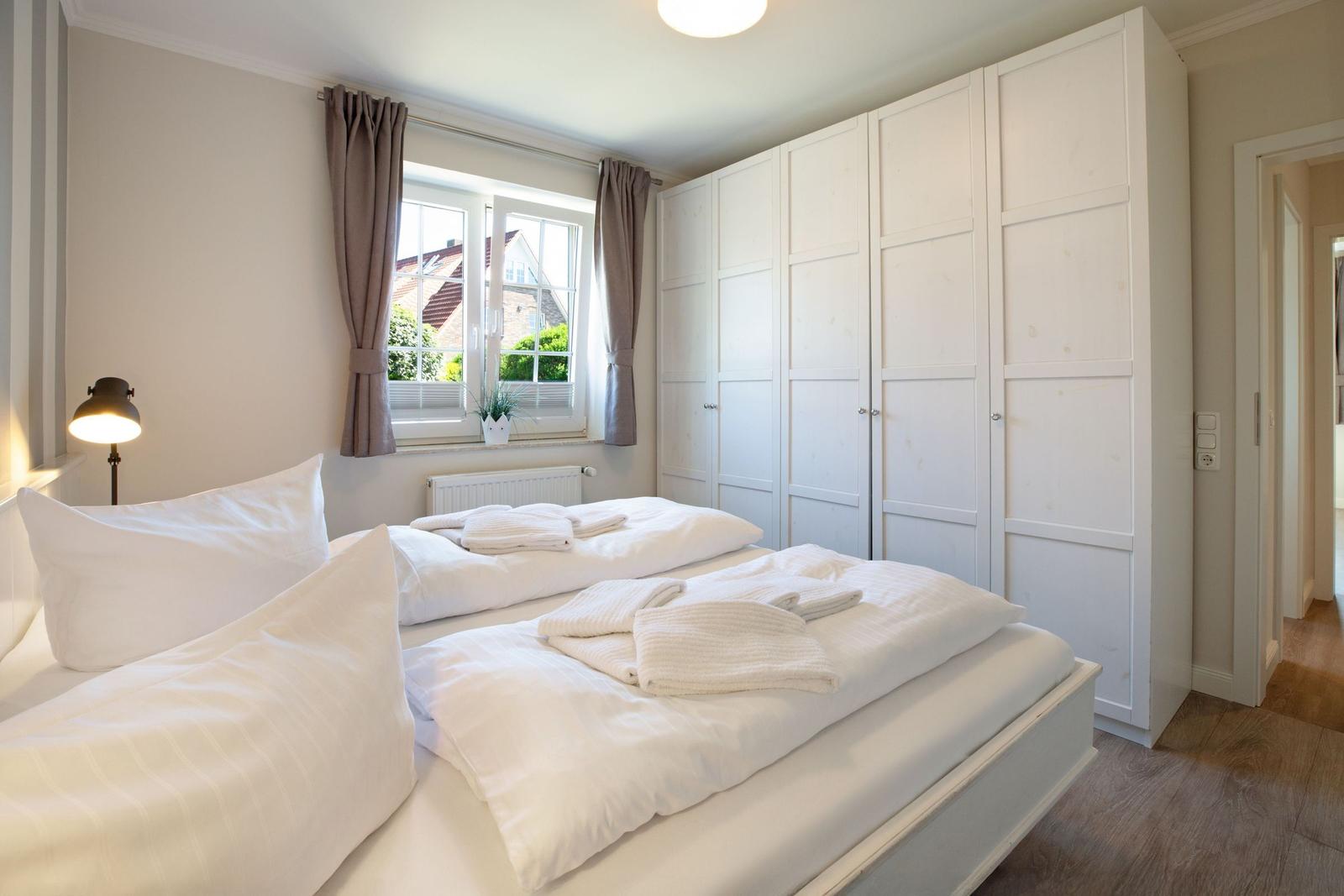 Schlafzimmer mit Doppelbett, weißen Bettwäsche, großen Schrank und Fenster mit Blick.