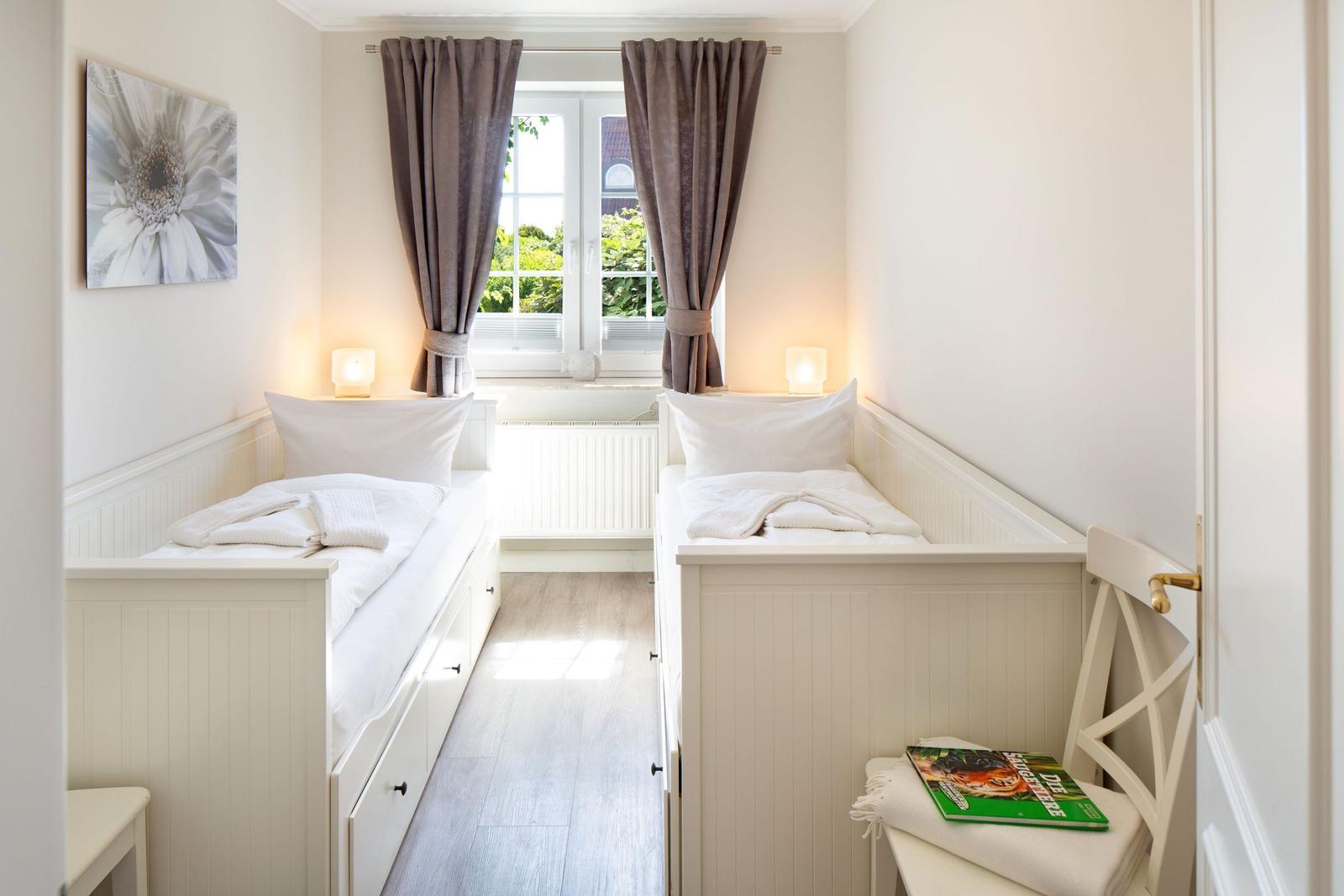 Zwei Einzelbetten mit weißen Laken, Fenster mit Vorhängen und Stühle im Raum.
