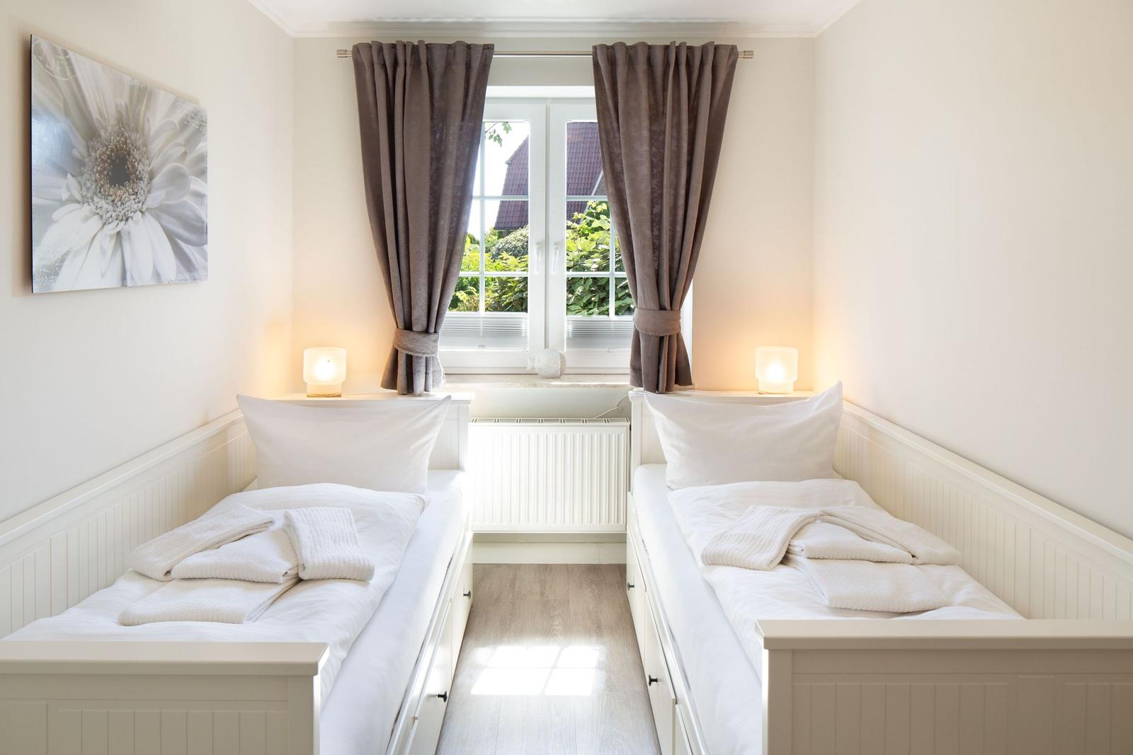 Zwei Betten mit weißen Laken und Handtüchern. Fenster mit braunen Vorhängen und Wandbild.