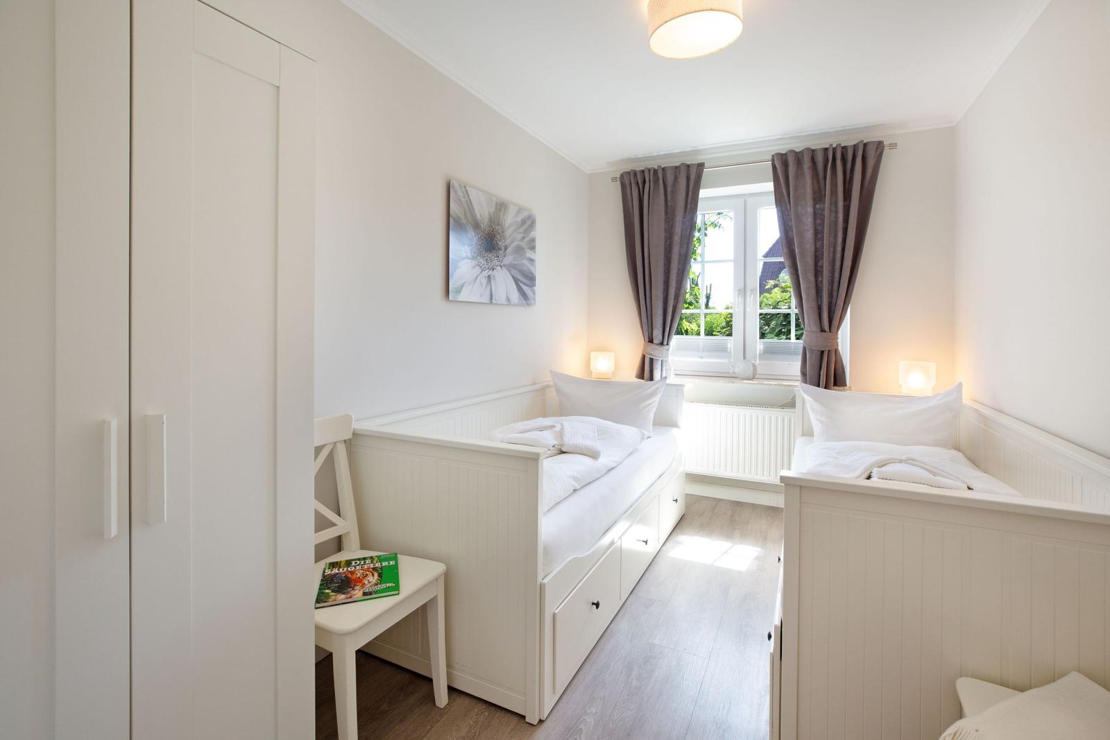 Zwei Einzelbetten mit weißen Laken, Fenster mit Vorhängen und Kleiderschrank.