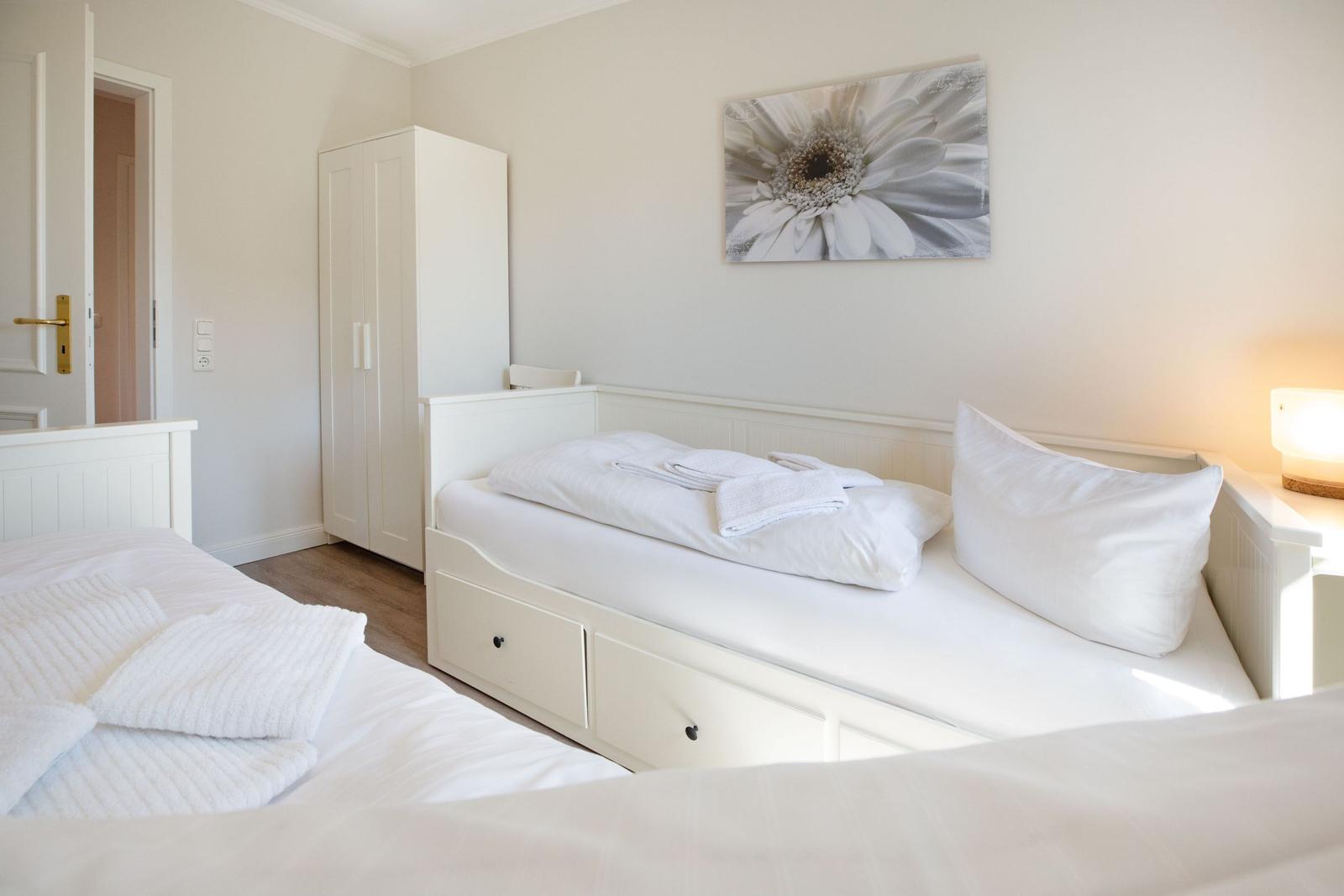 Zimmer mit zwei Betten, Schrank und Wandbild mit Blume.