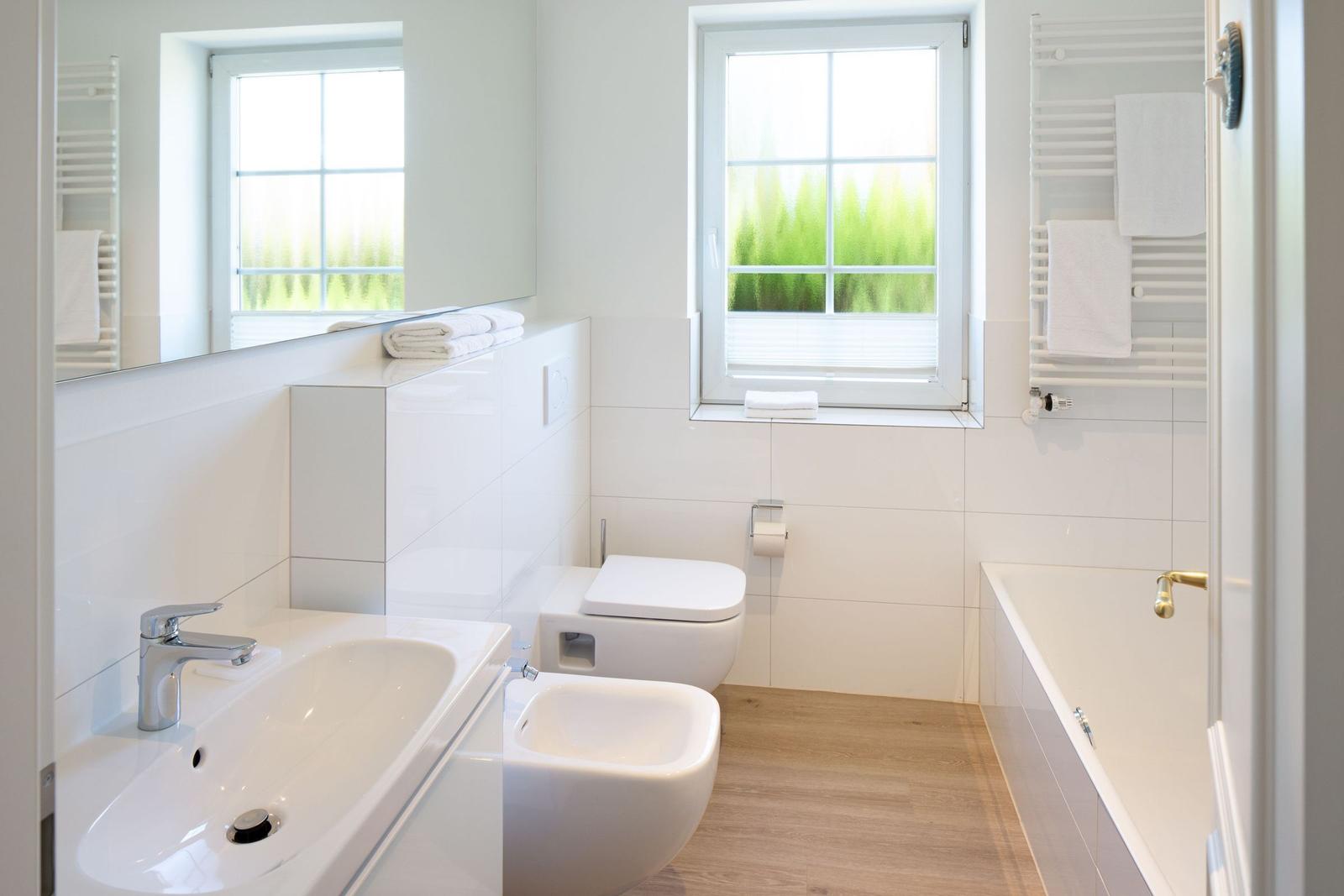 Badezimmer mit Badewanne, Toilette und Waschbecken. Fenster mit Blick auf Grün.