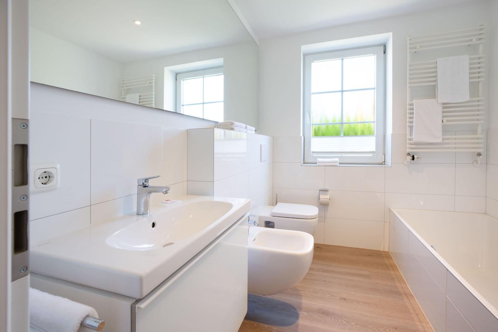 Badezimmer mit Waschbecken, Toilette, Bidet und Badewanne. Fenster mit Blick auf Grün.